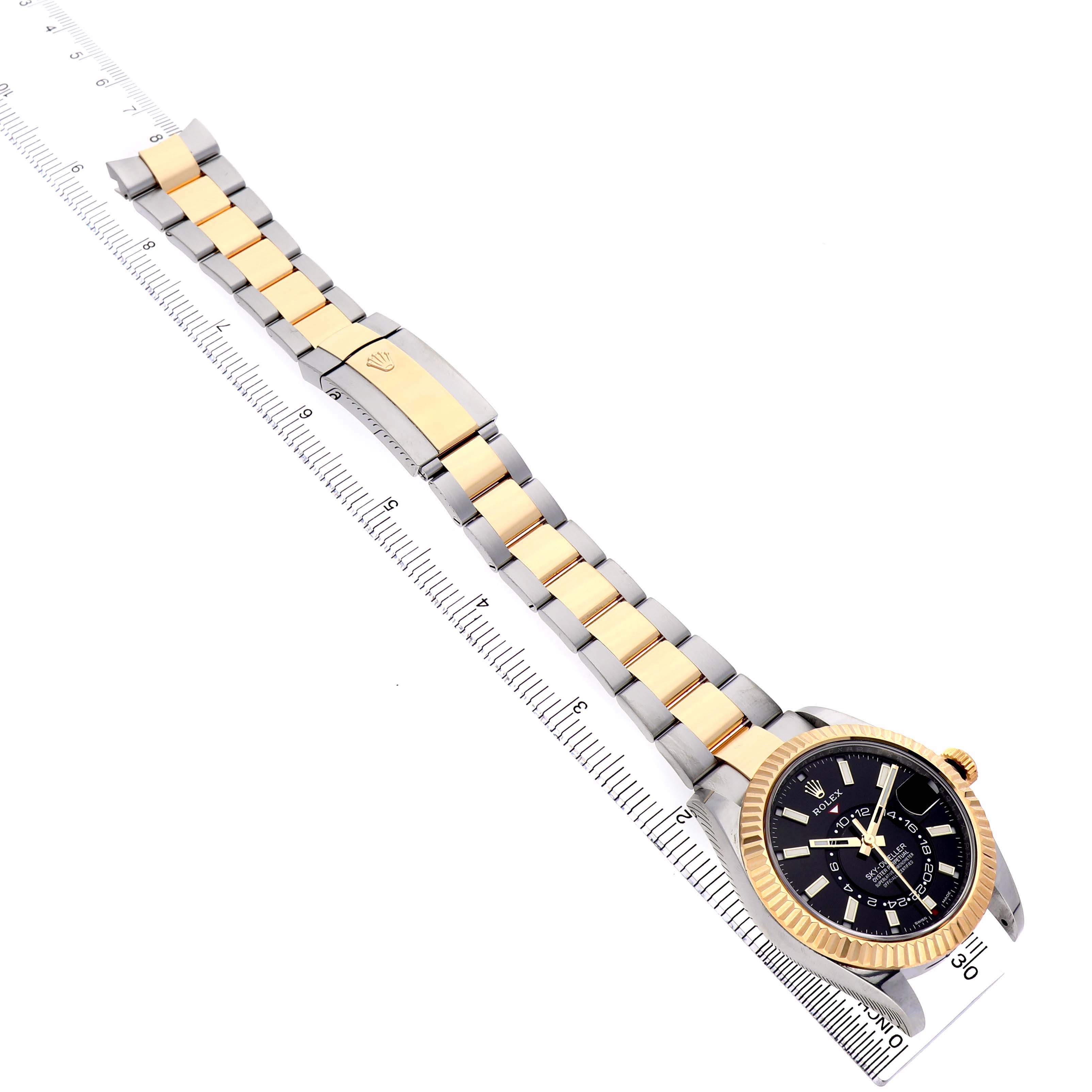 The image shows a Rolex Sky-Dweller 326933 Men's Steel and Gold (two tone) Black Dial watch from an elevated angle, highlighting the face, bracelet, and clasp, alongside a ruler for scale.