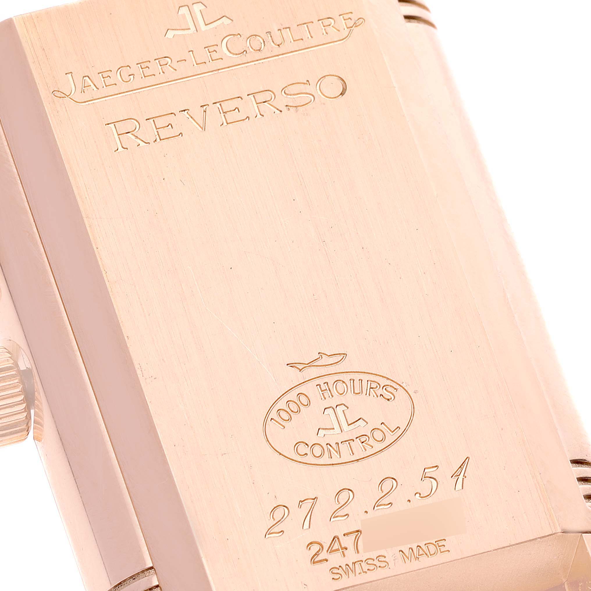 The image shows the engraved back of a Jaeger-LeCoultre Reverso watch at an angle, revealing brand, model, and quality control details.