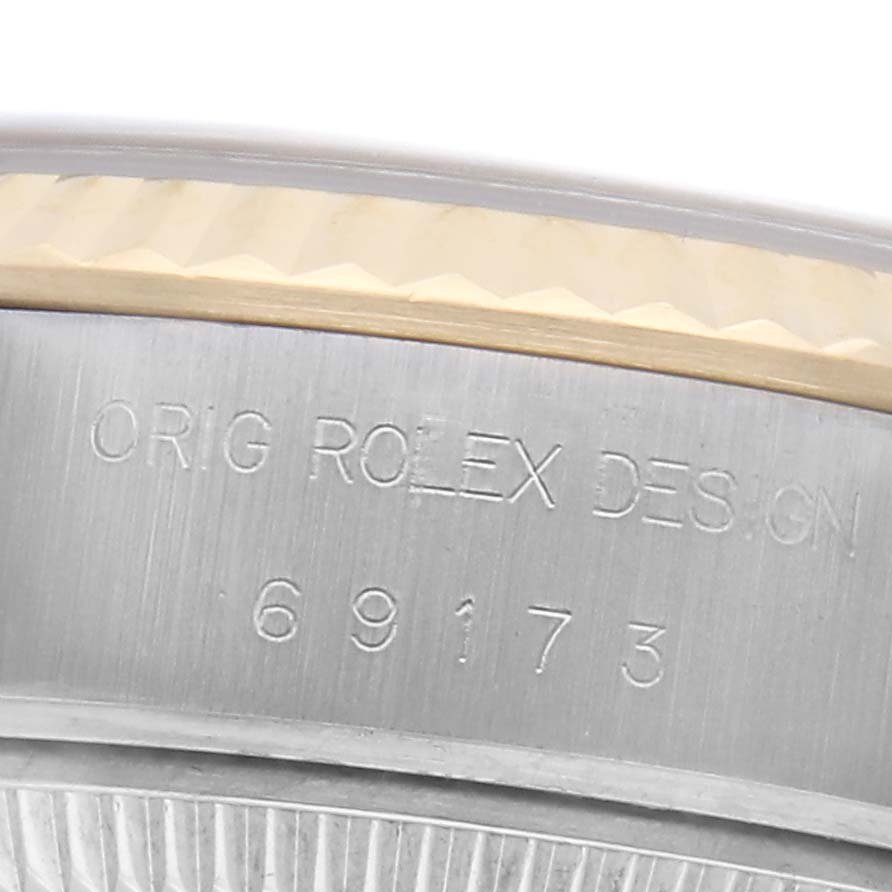 The image shows a close-up of the Rolex Datejust 69173 Women's Steel and Gold (two tone) White Dial 69173 Women's Steel and Gold (two tone) White Dial model's side, featuring engraving and part of the fluted bezel.