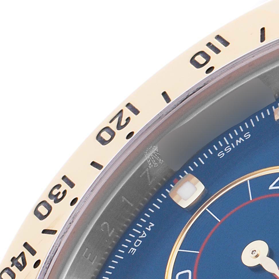 The image shows a close-up of the Rolex Daytona 116523 Men's Steel and Gold (two tone) Blue Dial 116523 Men's Steel and Gold (two tone) Blue Dial's bezel and part of its blue dial.