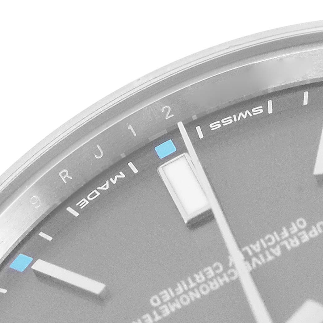 The image shows a close-up of the dial of a Rolex Oyster Perpetual 114300 Men's Stainless Steel Grey Dial 114300 Men's Stainless Steel Grey Dial watch, highlighting hour markers, part of the hands, and text.