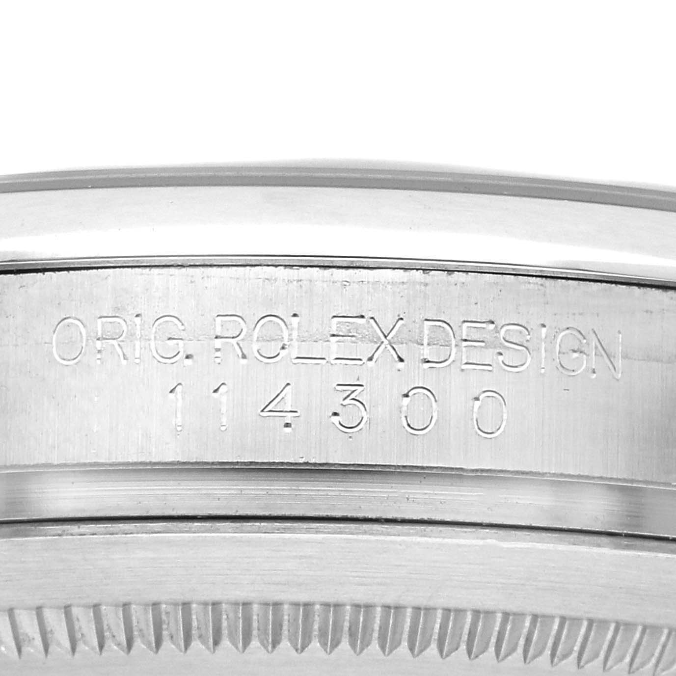 The image shows the side engraving of a Rolex Oyster Perpetual 114300 Men's Stainless Steel Grey Dial 114300 Men's Stainless Steel Grey Dial watch, featuring the model number and "Orig. Rolex Design."