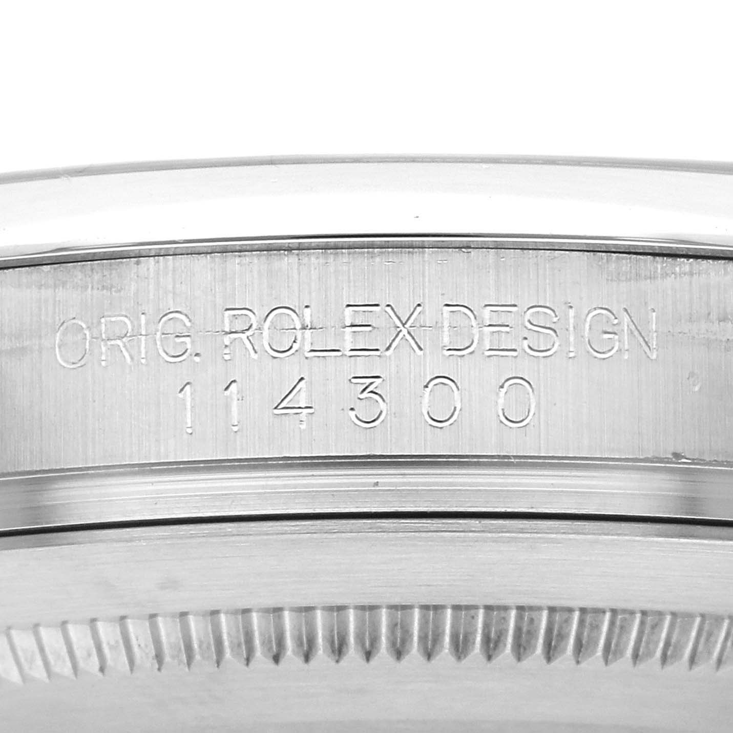 The image shows a close-up of the side engraving on a Rolex Oyster Perpetual 114300 Men's Stainless Steel Blue Dial 114300 Men's Stainless Steel Blue Dial model, displaying the design and model number.