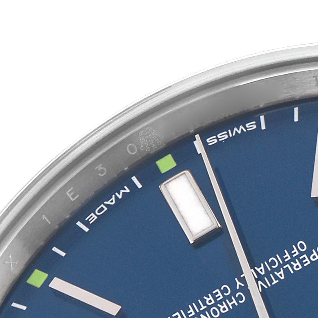 The image shows a close-up of the dial edge and markers of a Rolex Oyster Perpetual 114300 Men's Stainless Steel Blue Dial 114300 Men's Stainless Steel Blue Dial watch, focusing on the indices and lettering.