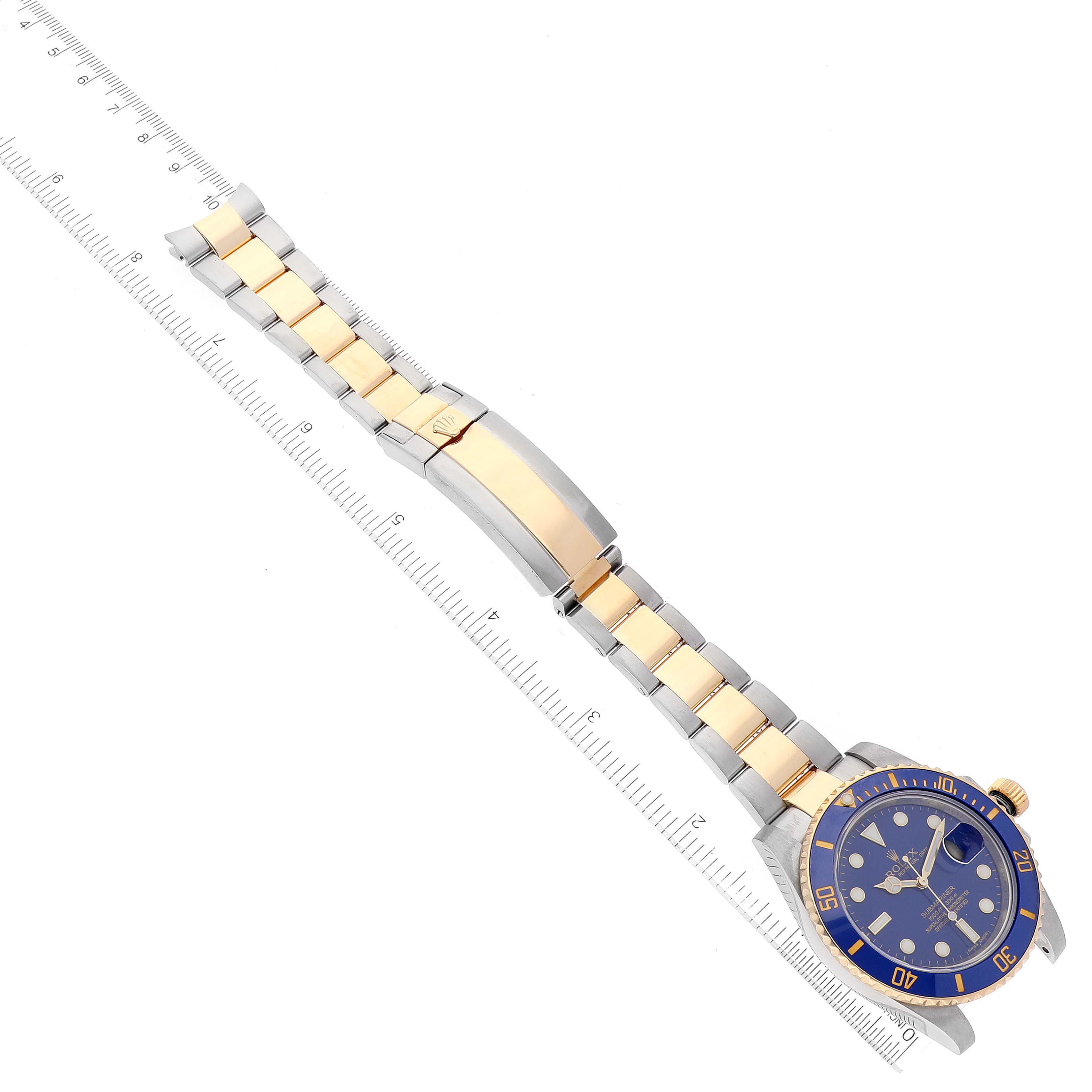 The image shows a Rolex Submariner 116613 Men's Steel and Gold (two tone) Blue Dial 116613 Men's Steel and Gold (two tone) Blue Dial watch laid flat at an overhead angle, displaying the face, bezel, and entire bracelet alongside a ruler.