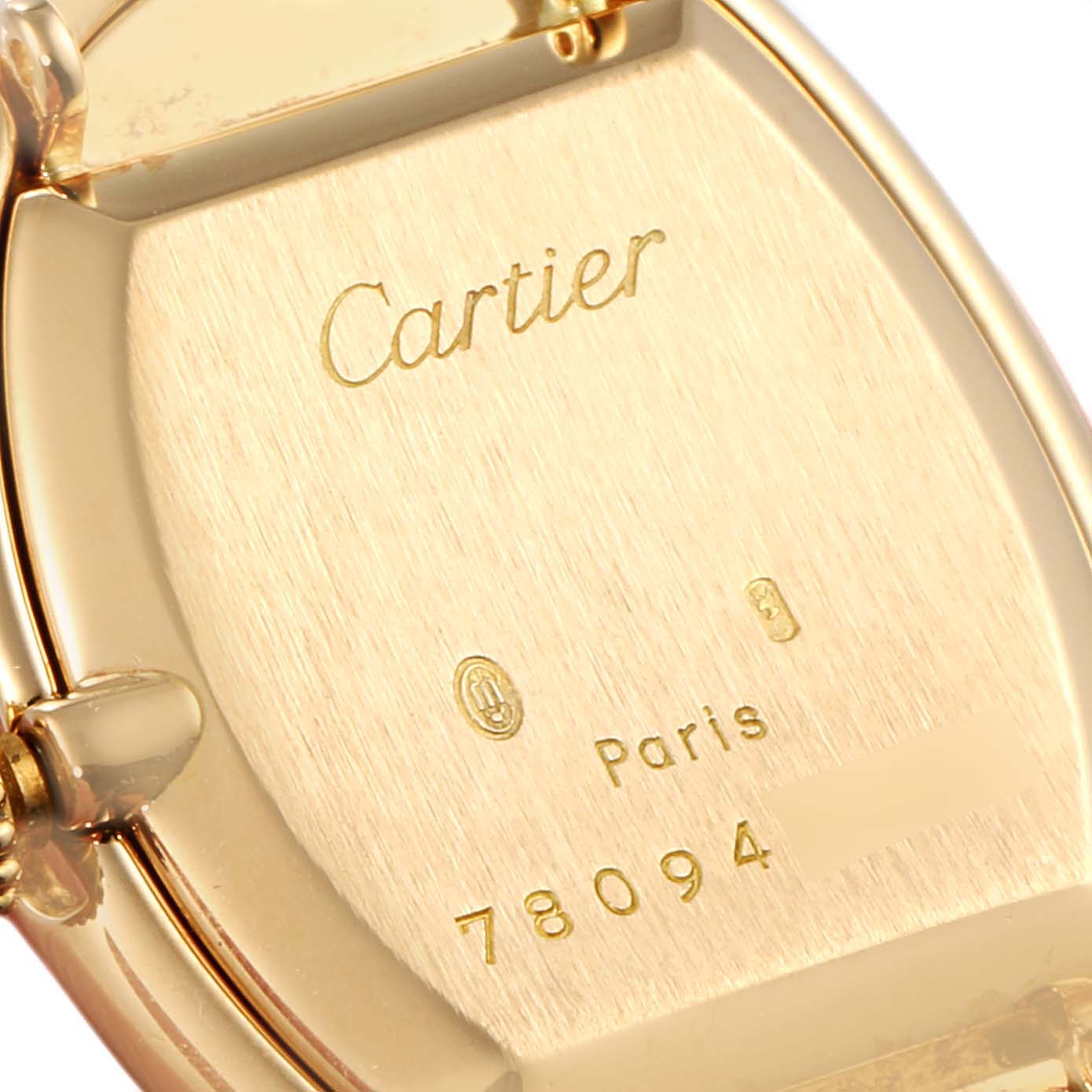 The image shows the back case of a Cartier Baignoire Women's Yellow Gold White Dial Women's Yellow Gold White Dial watch, highlighting the brand name, serial number, and marks.