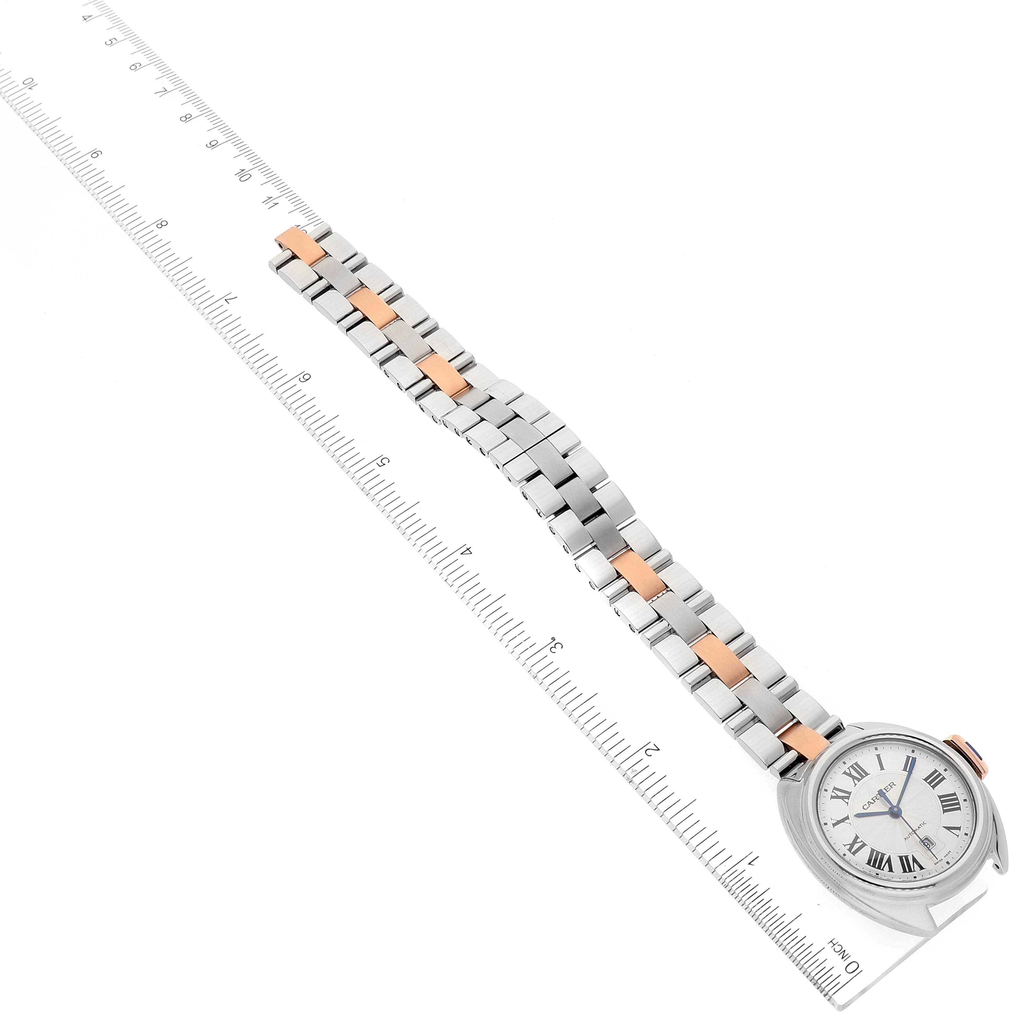 The image shows the Cartier Clé watch from a top-down angle, displaying the watch face, bracelet, and a measuring ruler.
