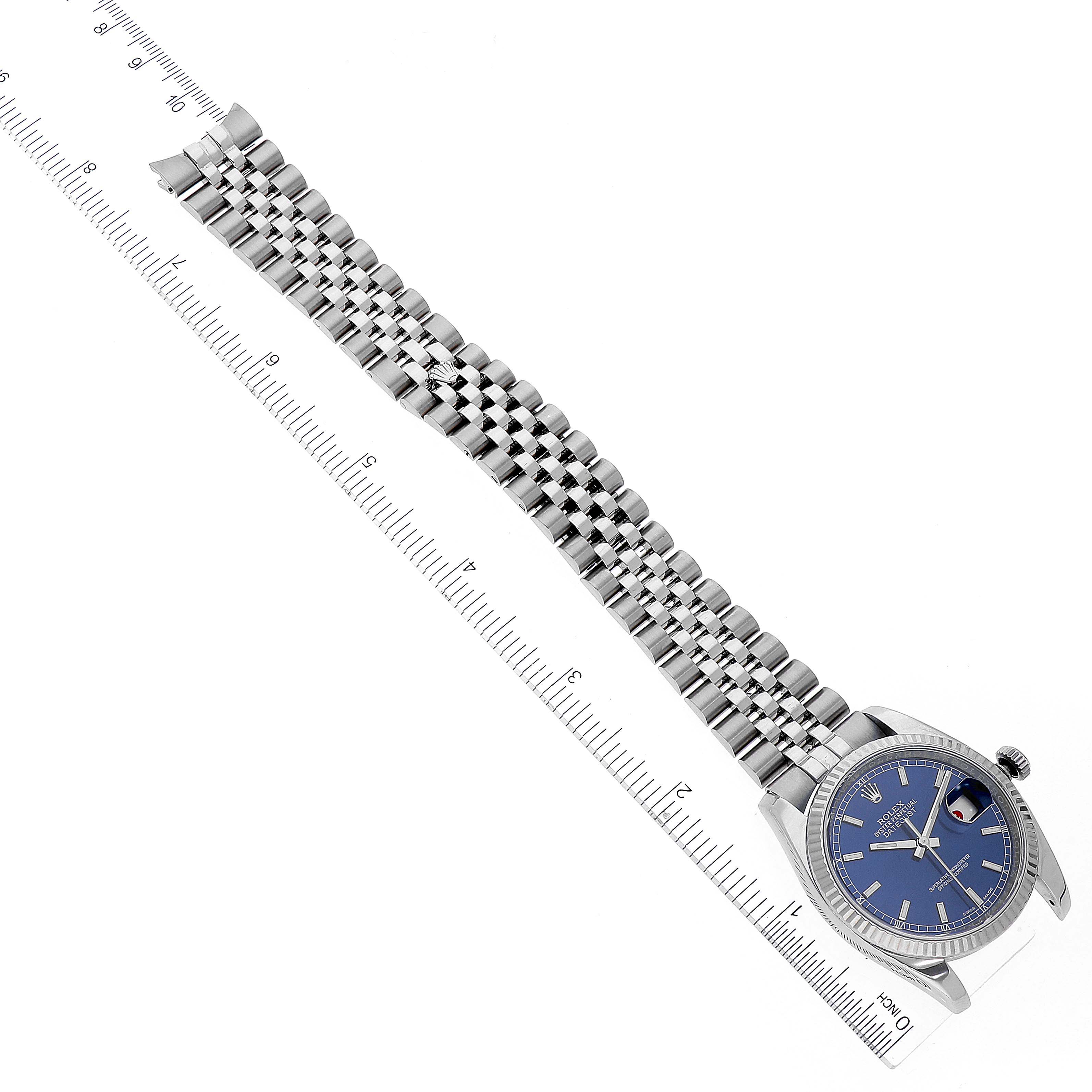 The image shows a Rolex Datejust 116234 Men's Stainless Steel Blue Dial 116234 Men's Stainless Steel Blue Dial watch laid flat, displaying its blue dial, fluted bezel, and Jubilee bracelet with a ruler for scale.