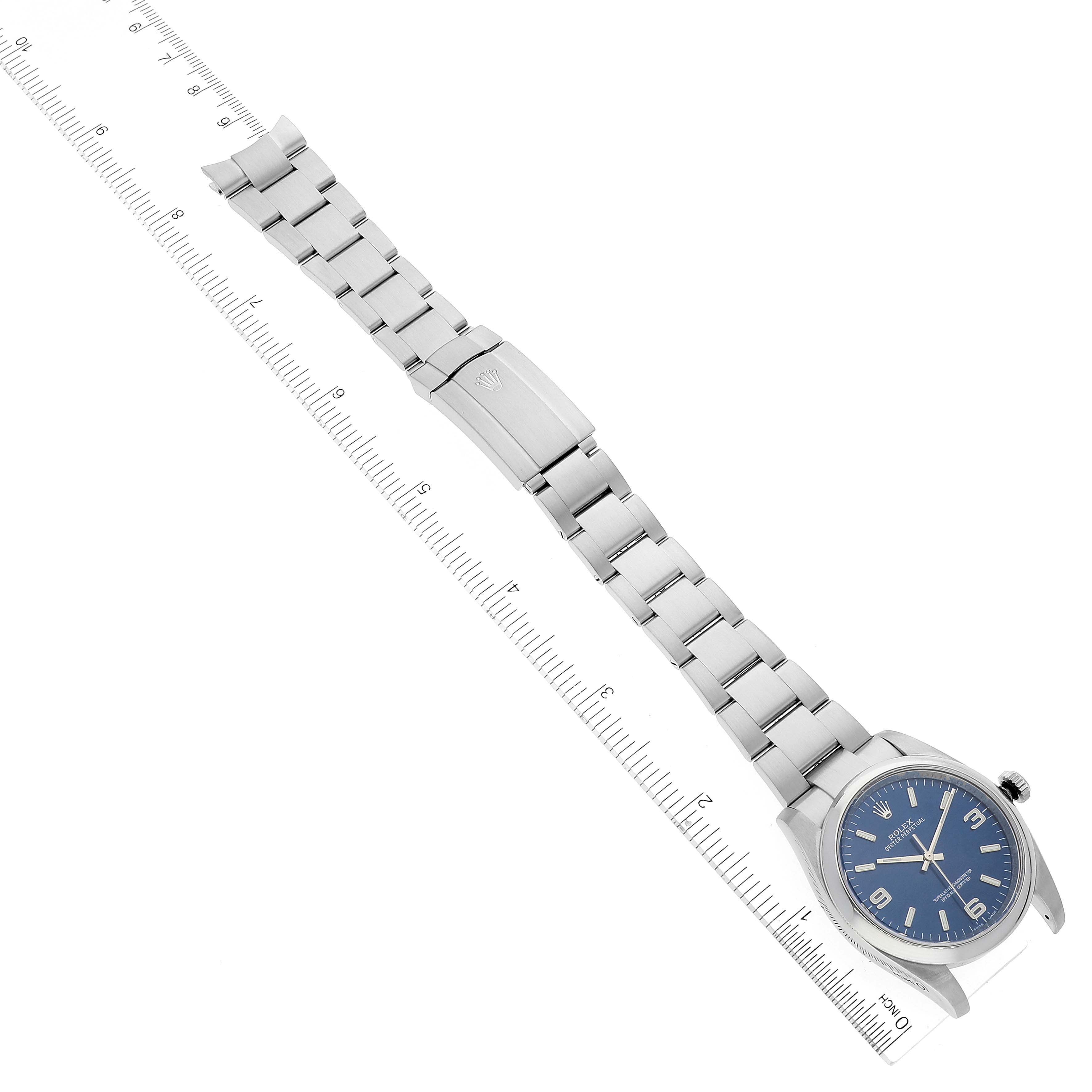 The image shows a Rolex Oyster Perpetual 116000 Men's Stainless Steel Blue Dial 116000 Men's Stainless Steel Blue Dial watch laid flat with its bracelet fully extended, alongside a ruler.
