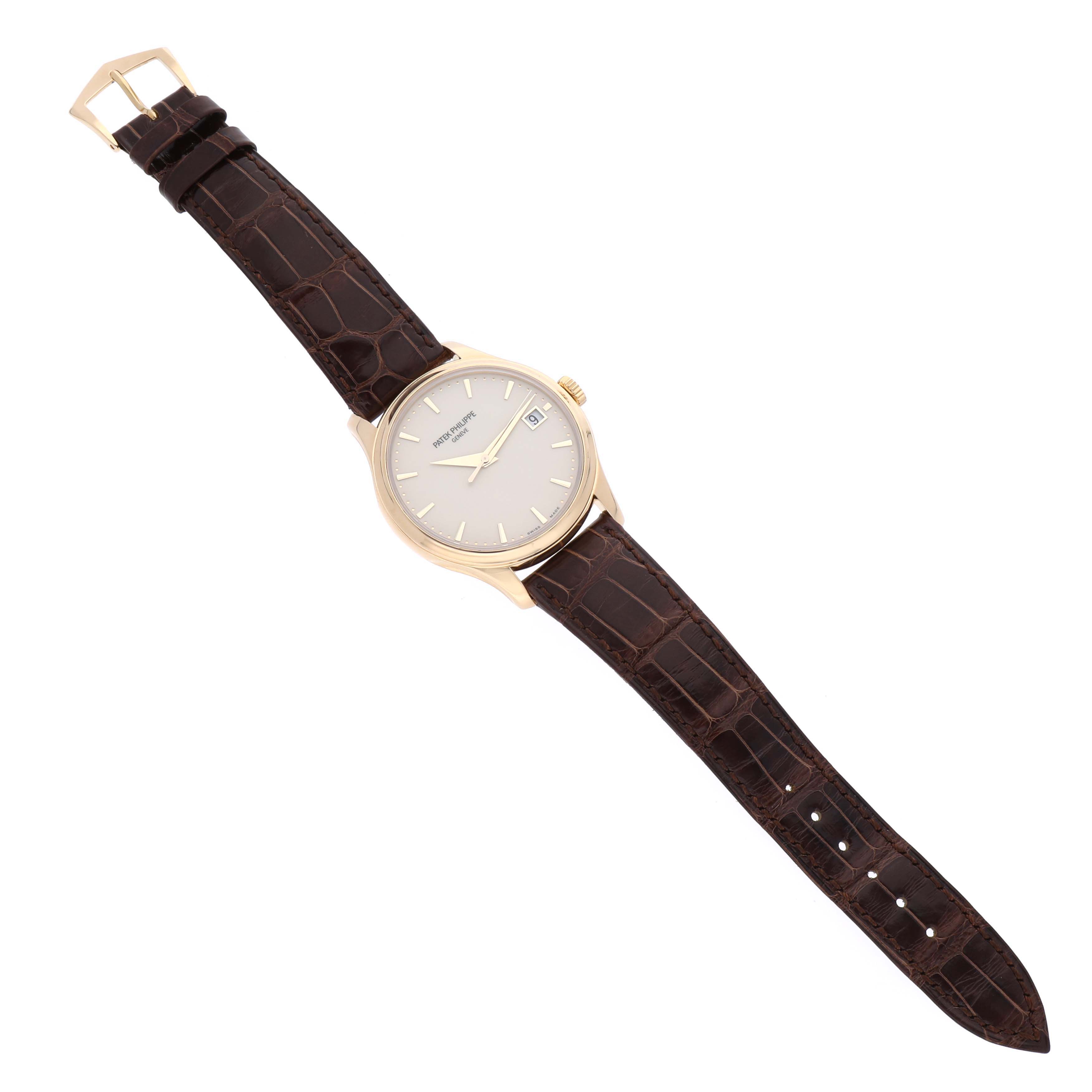 The image shows a top view of a Patek Philippe Calatrava 5227J Men's Yellow Gold White Dial 5227J Men's Yellow Gold White Dial watch with a brown leather strap and gold case.