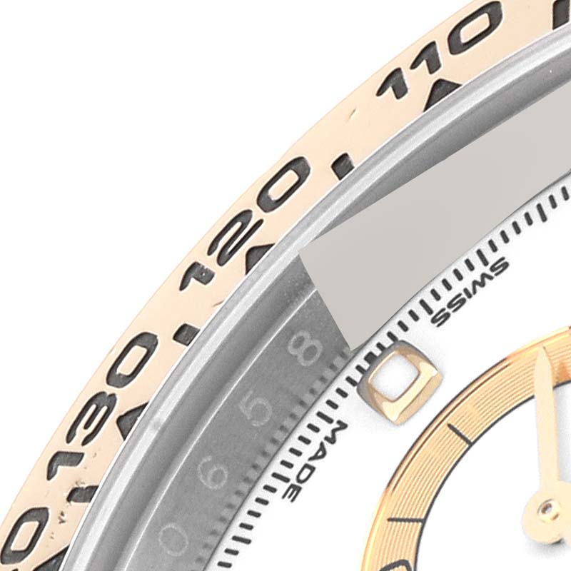 This close-up of a Rolex Daytona 116503 Men's Steel and Gold (two tone) White Dial 116503 Men's Steel and Gold (two tone) White Dial watch shows part of the bezel, dial, and hour markers from an angled view.
