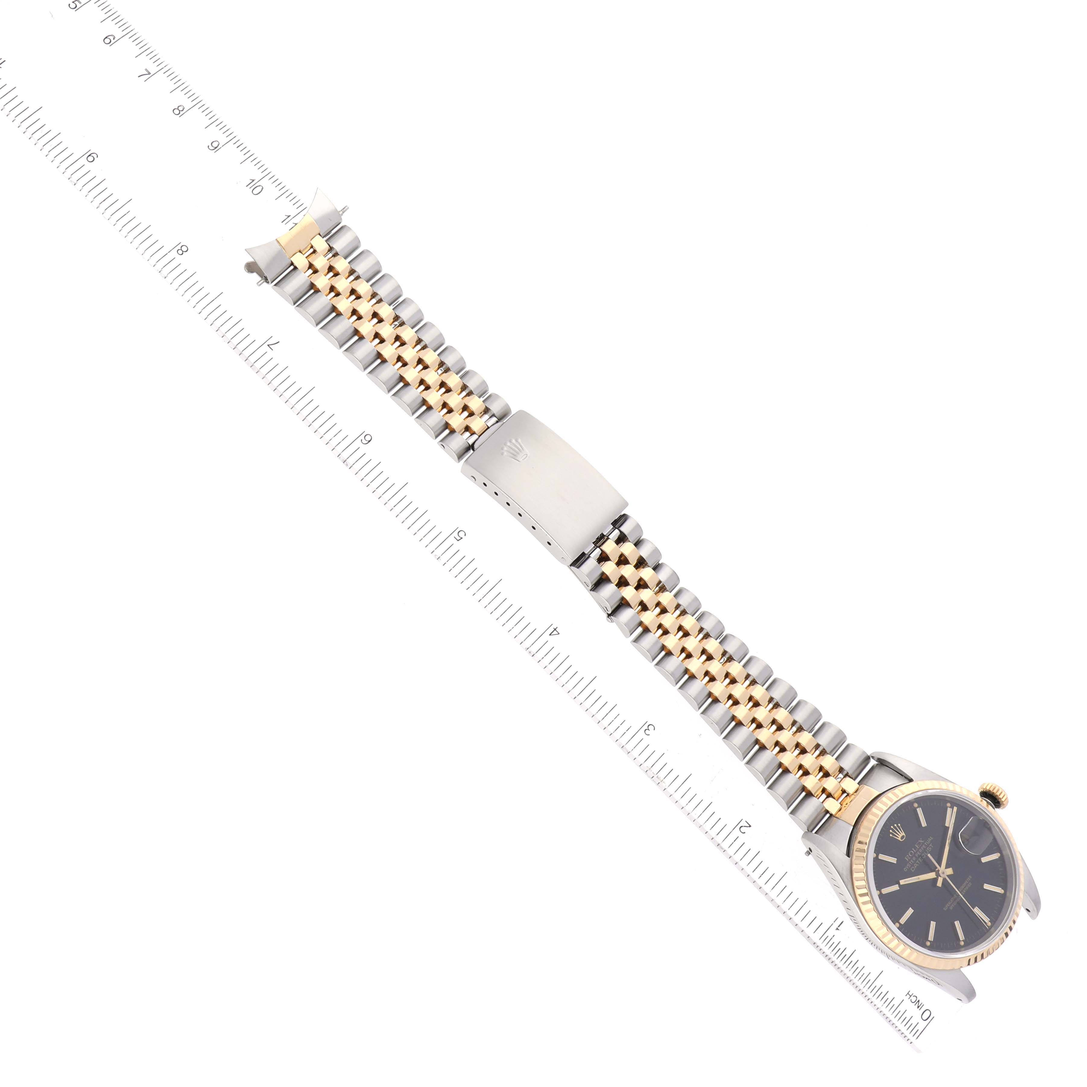 This image shows the Rolex Datejust 16233 Men's Steel and Gold (two tone) Black Dial 16233 Men's Steel and Gold (two tone) Black Dial watch laid flat alongside a ruler, highlighting its band and face from an overhead angle.