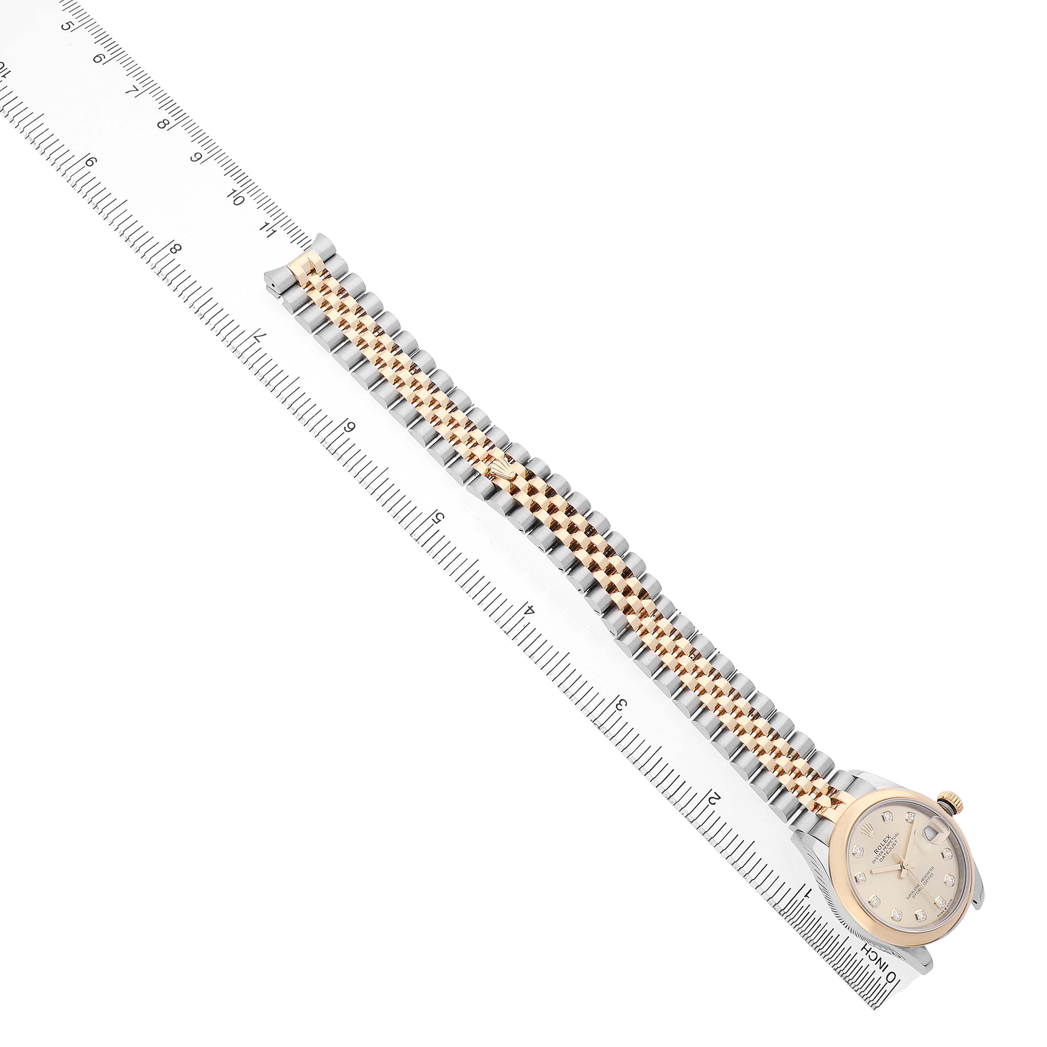 The Rolex Mid-Size 278243 Women's Steel and Gold (two tone) Champagne Dial watch is shown from an overhead angle, highlighting the watch face, bracelet, and crown, alongside a ruler.