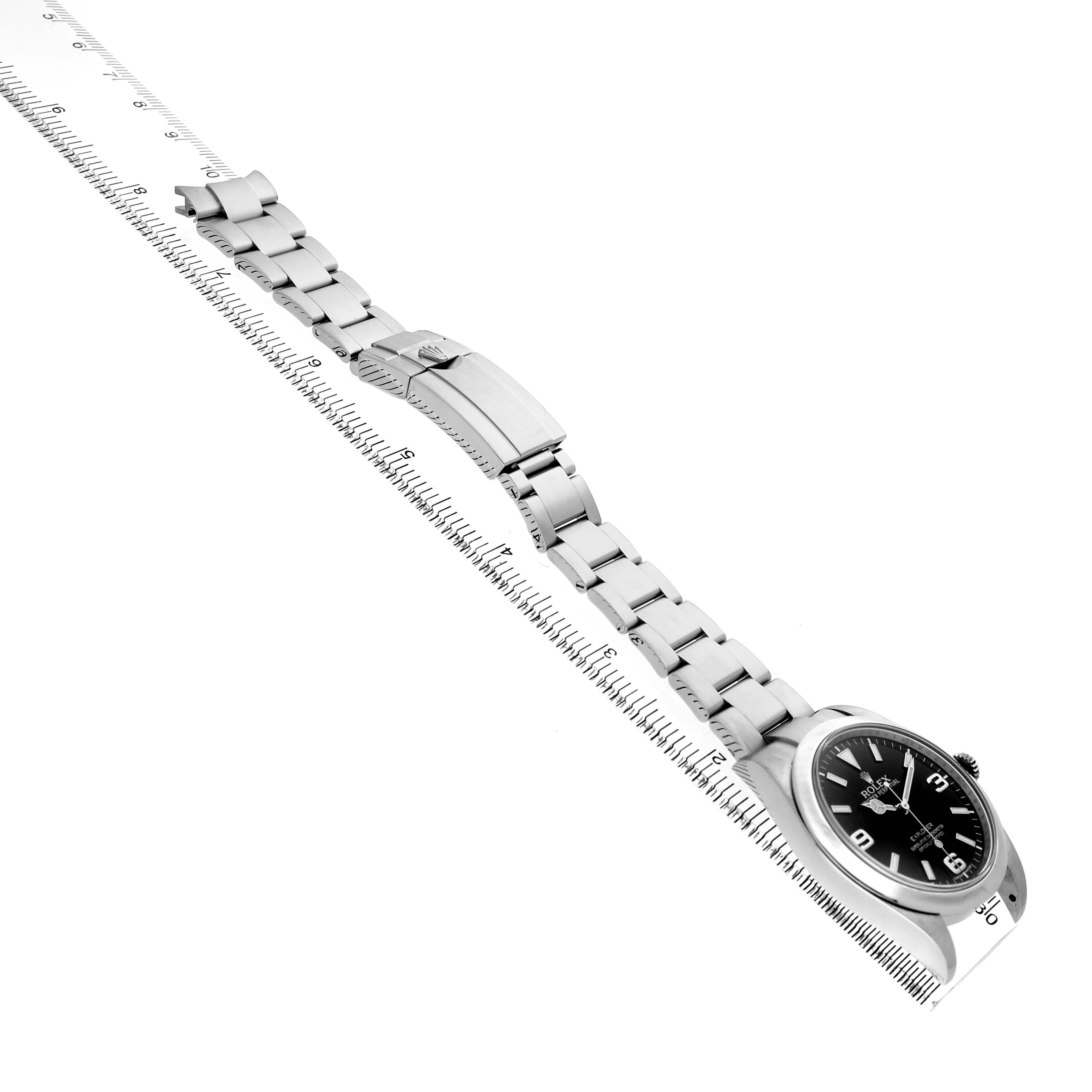 The Rolex Explorer 214270 Men's Stainless Steel Black Dial watch is shown side-on, highlighting its bracelet, clasp, and watch face, with a ruler for scale.