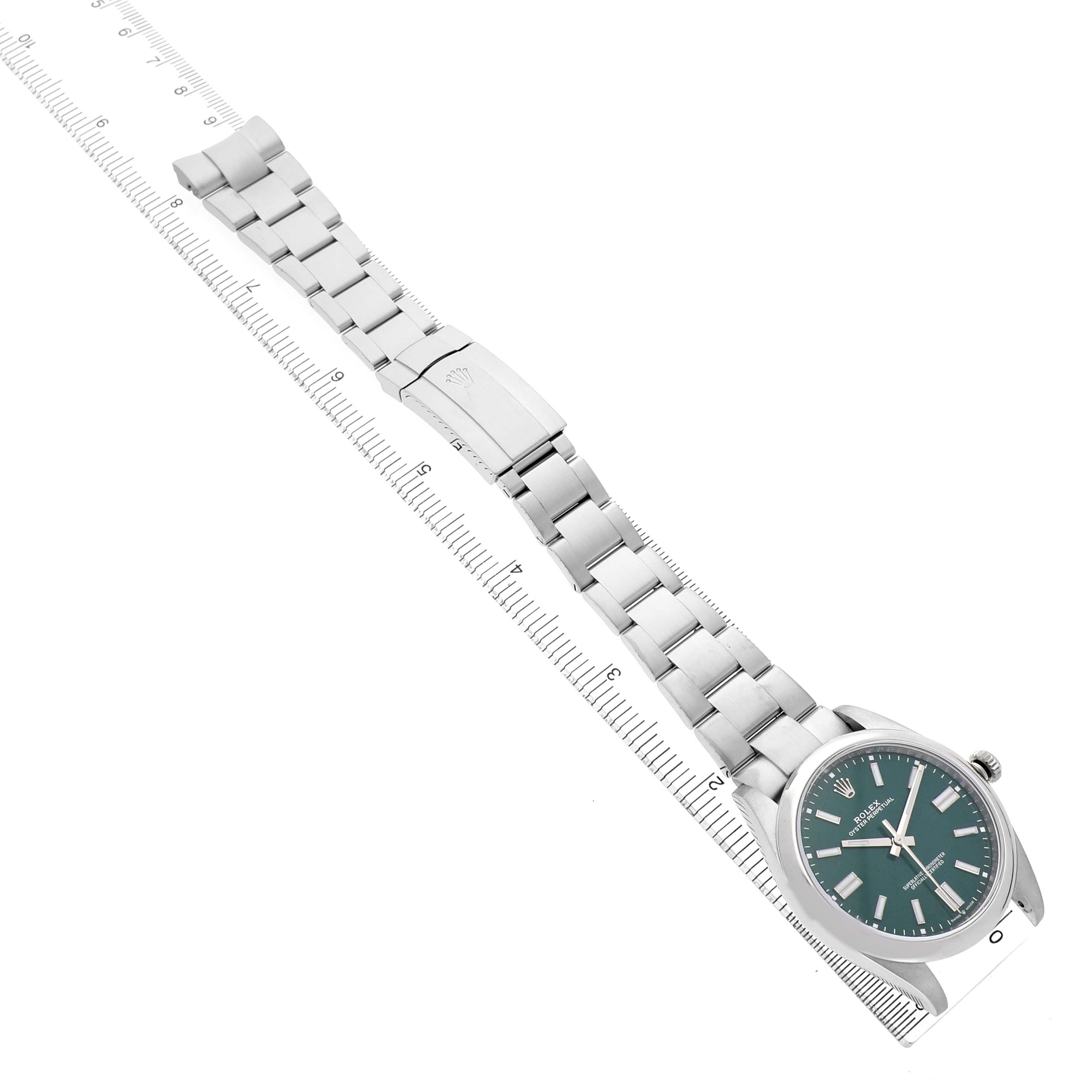 The Rolex Oyster Perpetual M124300-0005 Men's Stainless Steel Green Dial watch is shown from a top-down angle, displaying the face, bracelet, and clasp on a ruler.