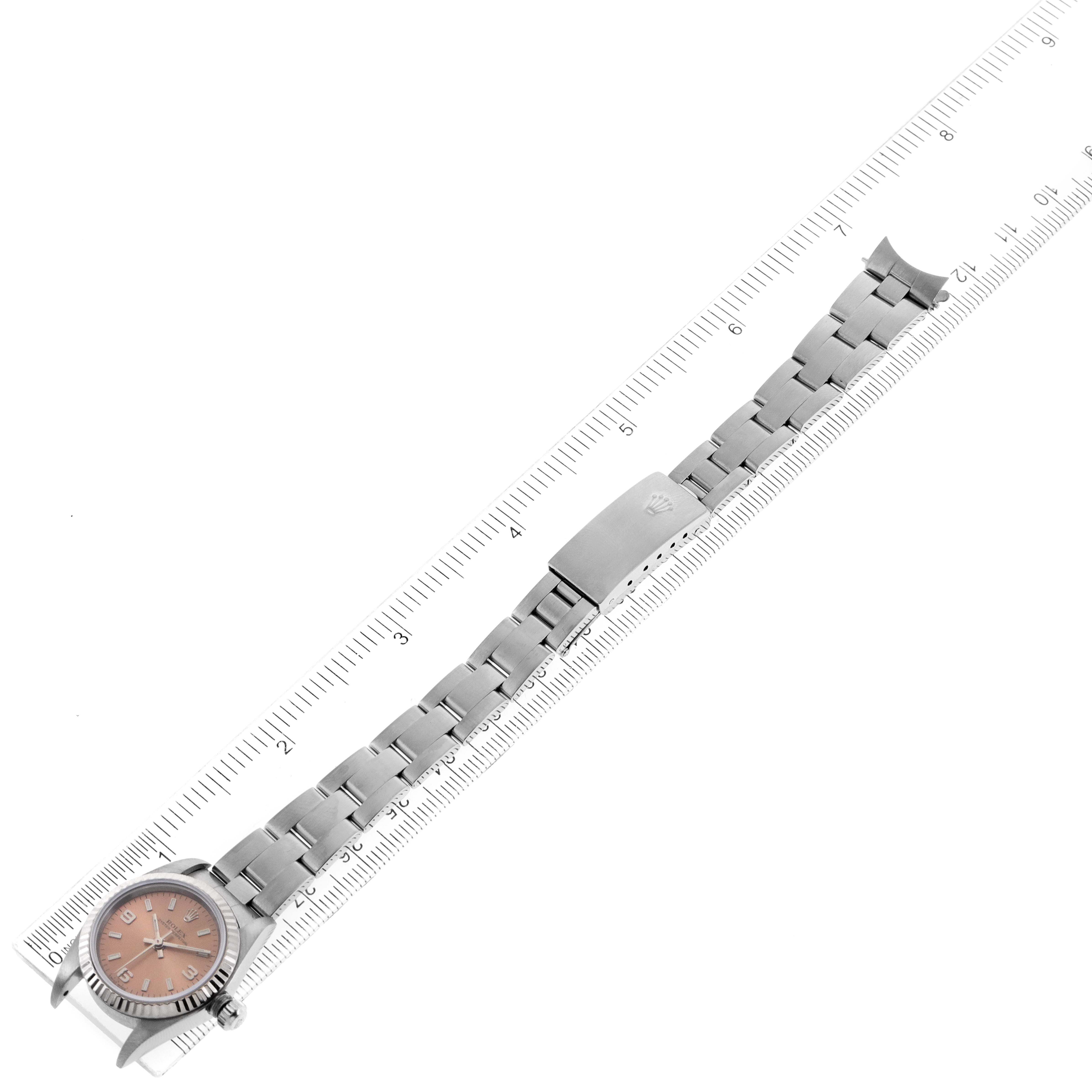 The Rolex Oyster Perpetual 76094 Women's Stainless Steel Pink Dial 76094 Women's Stainless Steel Pink Dial watch is shown fully extended with a ruler for scale, highlighting its face, bracelet, and clasp.