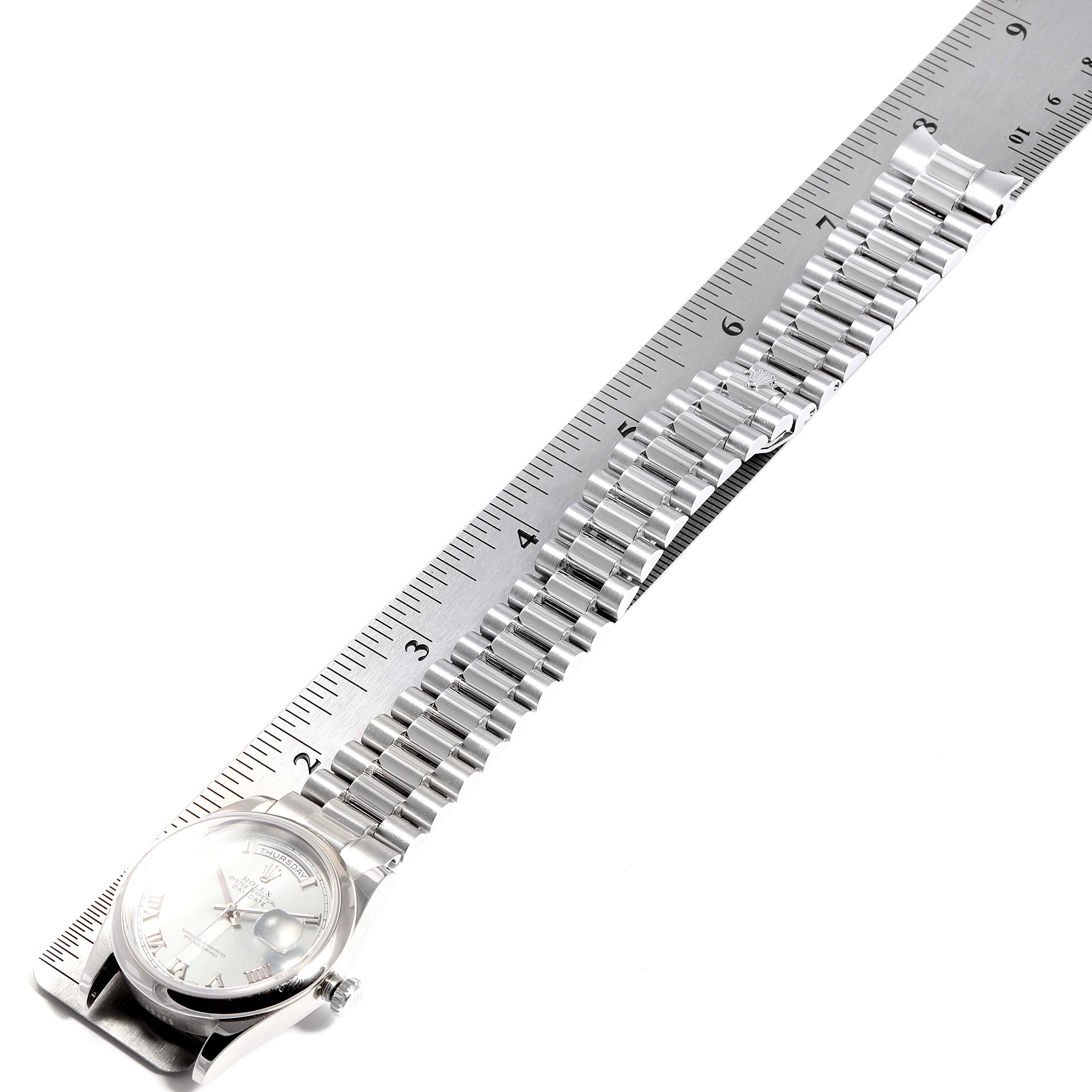 The angle shows the front side of the Rolex President 118206 Men's Platinum Blue Dial 118206 Men's Platinum Blue Dial model watch and its full metal band, lying against a ruler.