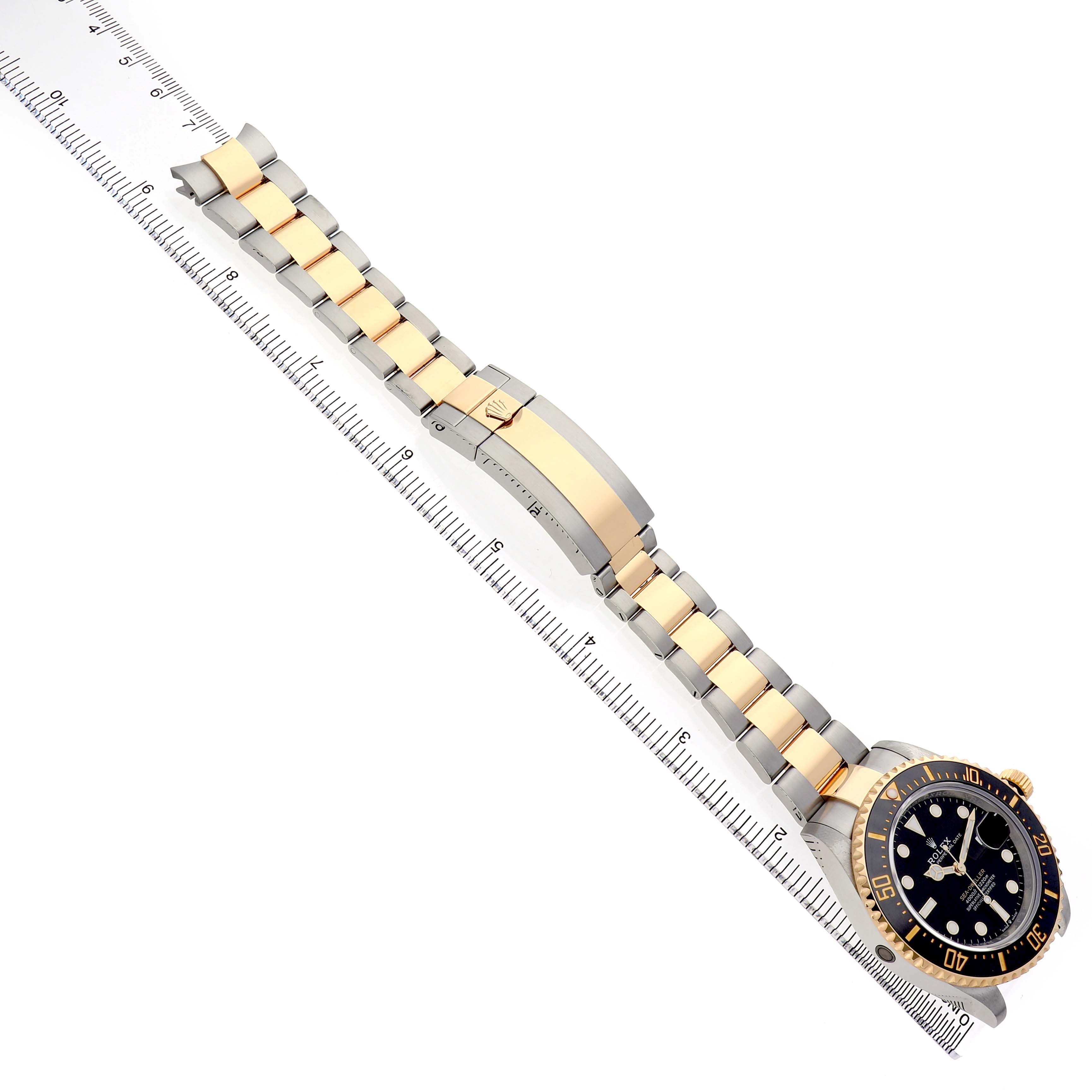 The Rolex Sea-Dweller M126603 Men's Steel and Gold (two tone) Black Dial watch is shown at an angle, displaying its face, case, and bracelet against a ruler for scale.