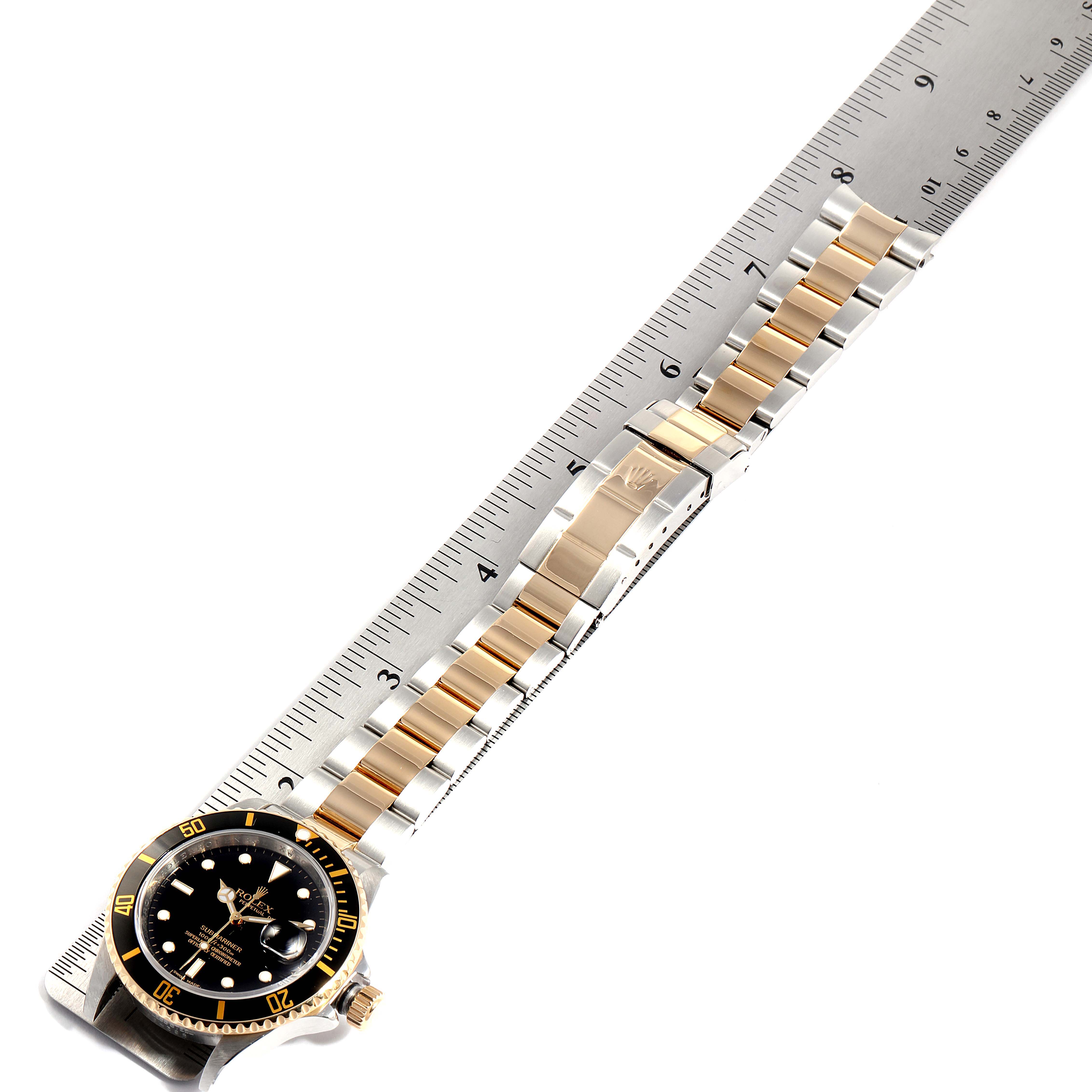 The image shows a Rolex Submariner 16613 Men's Steel and Gold (two tone) Black Dial 16613 Men's Steel and Gold (two tone) Black Dial watch laid flat alongside a ruler, displaying the dial, bezel, crown, and two-tone bracelet.