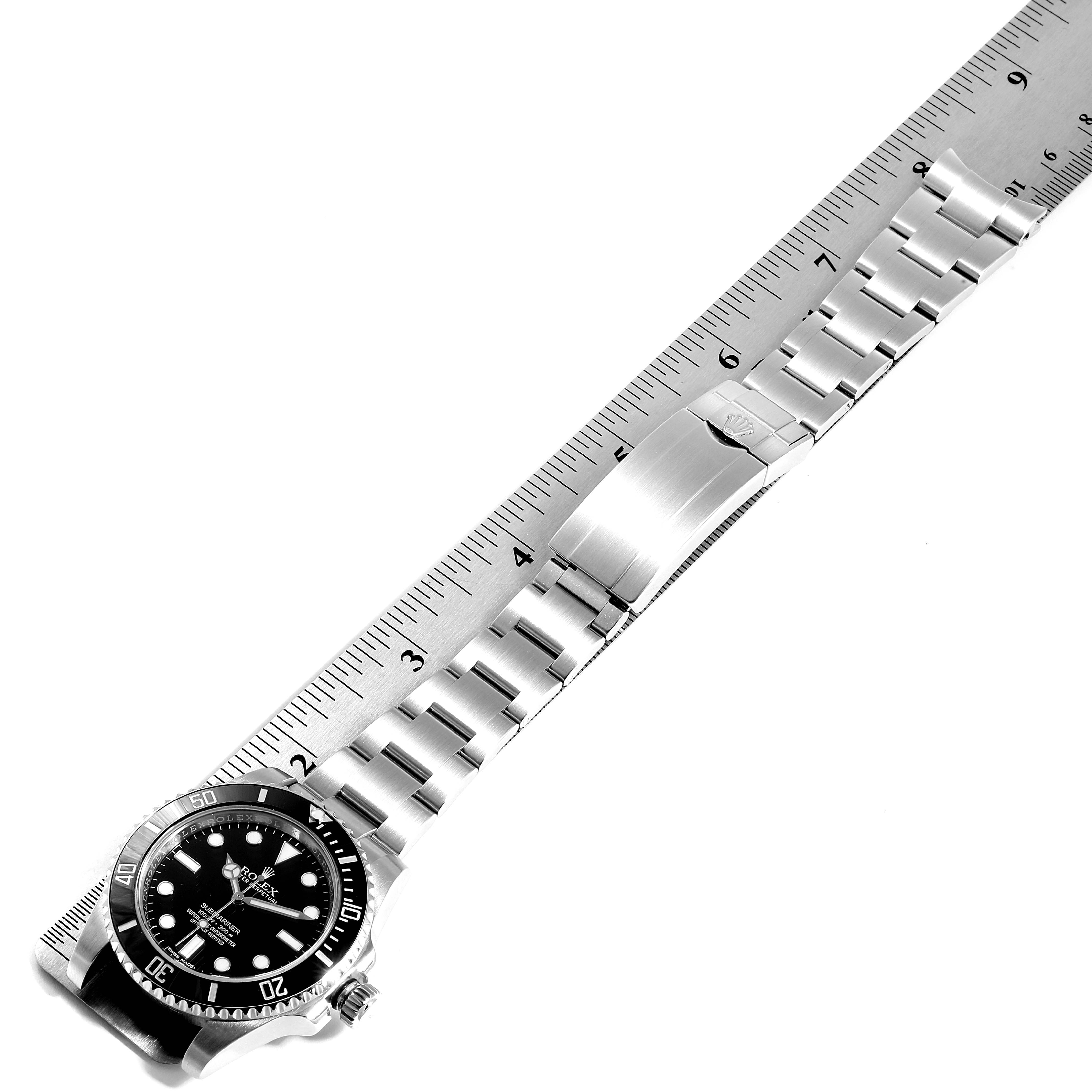 This Rolex Submariner 114060 Men
s Stainless Steel Black Dial 114060 Men
s Stainless Steel Black Dial watch is shown from a top-down angle, displaying the full length of the band, clasp, and face next to a ruler.