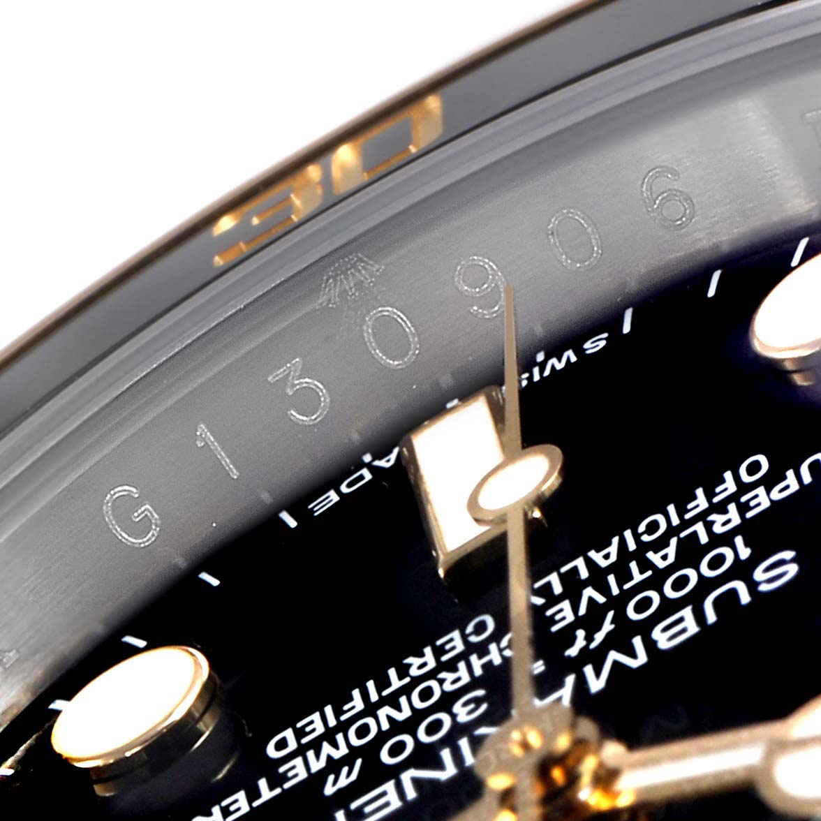 This close-up image of the Rolex Submariner 116613 Men
s Steel and Gold (two tone) Black Dial 116613 Men
s Steel and Gold (two tone) Black Dial watch shows part of the dial, inscriptions, and the watch hands.