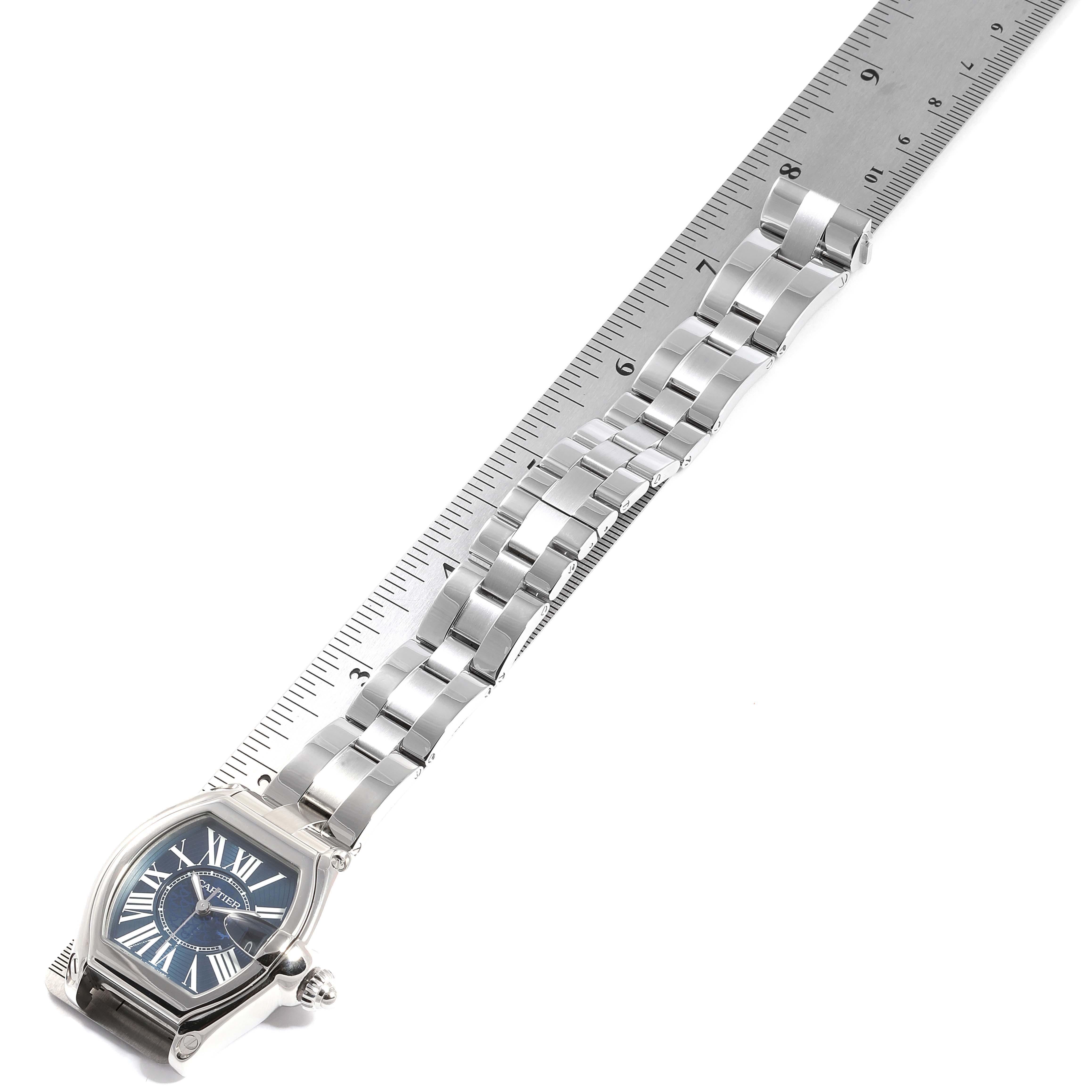 The image shows a Cartier Roadster W6206012 Men
s Stainless Steel Blue Dial W6206012 Men
s Stainless Steel Blue Dial watch with its face and entire metal bracelet aligned next to a ruler for measurement.