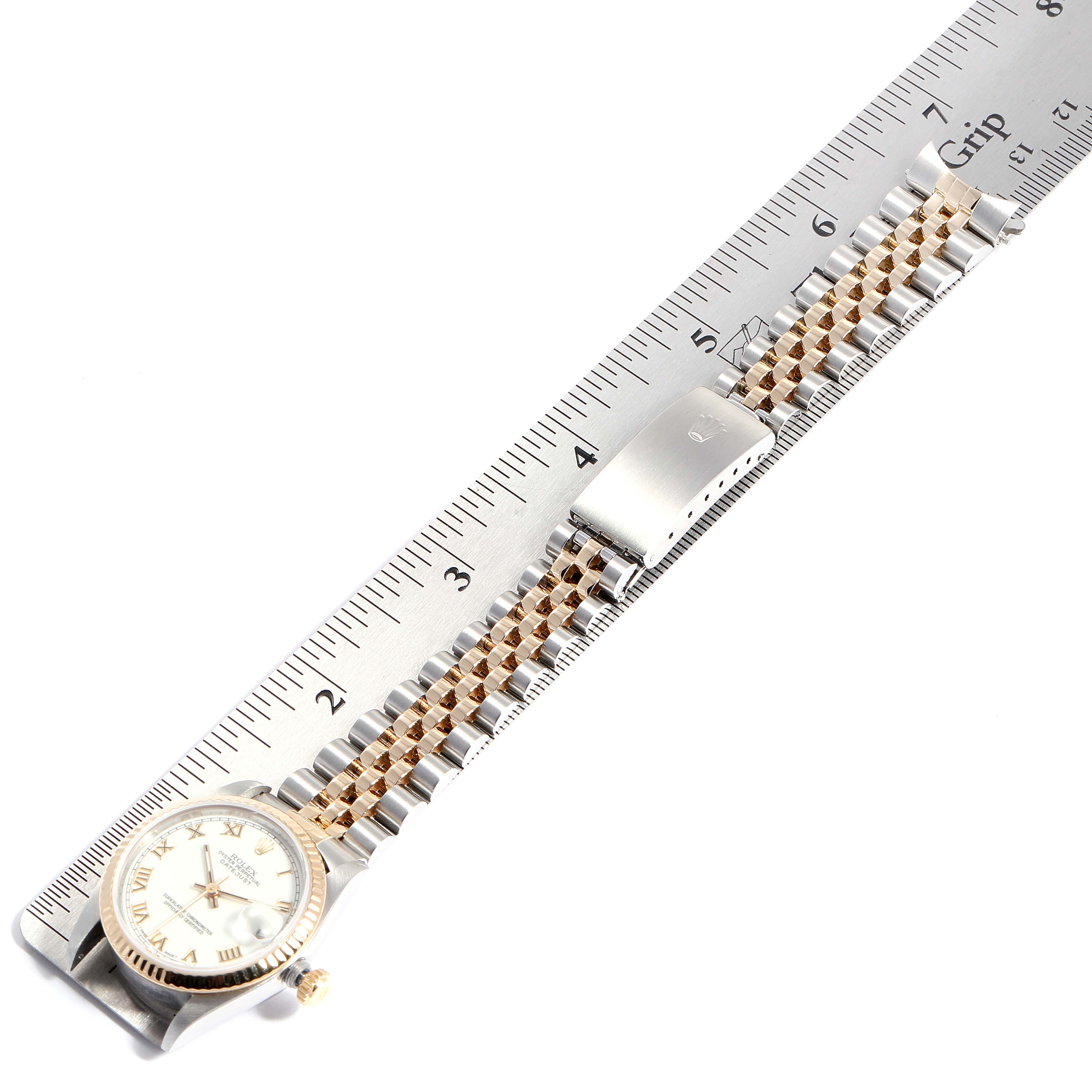 The Rolex Mid-Size 68273 Women
s Steel and Gold (two tone) White Dial 68273 Women
s Steel and Gold (two tone) White Dial watch is shown from a top view, highlighting its face, bracelet, and secured clasp next to a measuring ruler.