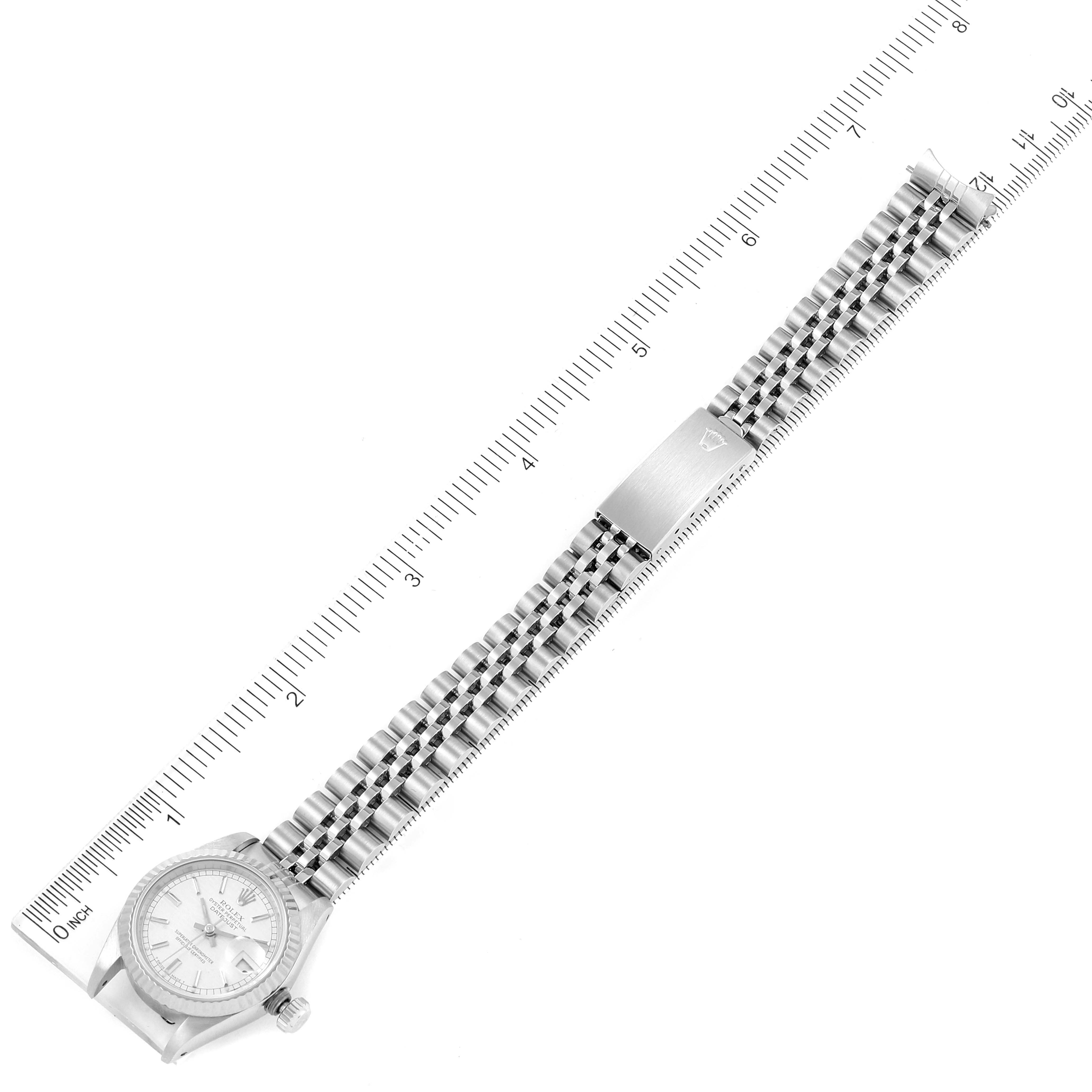 The Rolex Datejust 69174 Women
s Stainless Steel Silver Dial 69174 Women
s Stainless Steel Silver Dial watch is shown from an overhead angle, featuring the dial, bracelet, and clasp, aligned next to a measuring scale.