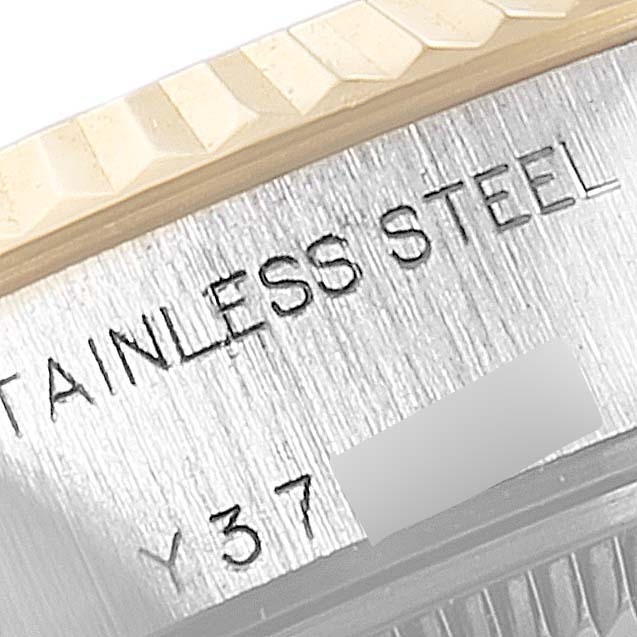 This close-up of a Rolex Datejust 79173 Women's Steel and Gold (two tone) Black Dial 79173 Women's Steel and Gold (two tone) Black Dial watch shows part of the stainless steel casing with engraved text and the edge of the fluted bezel.
