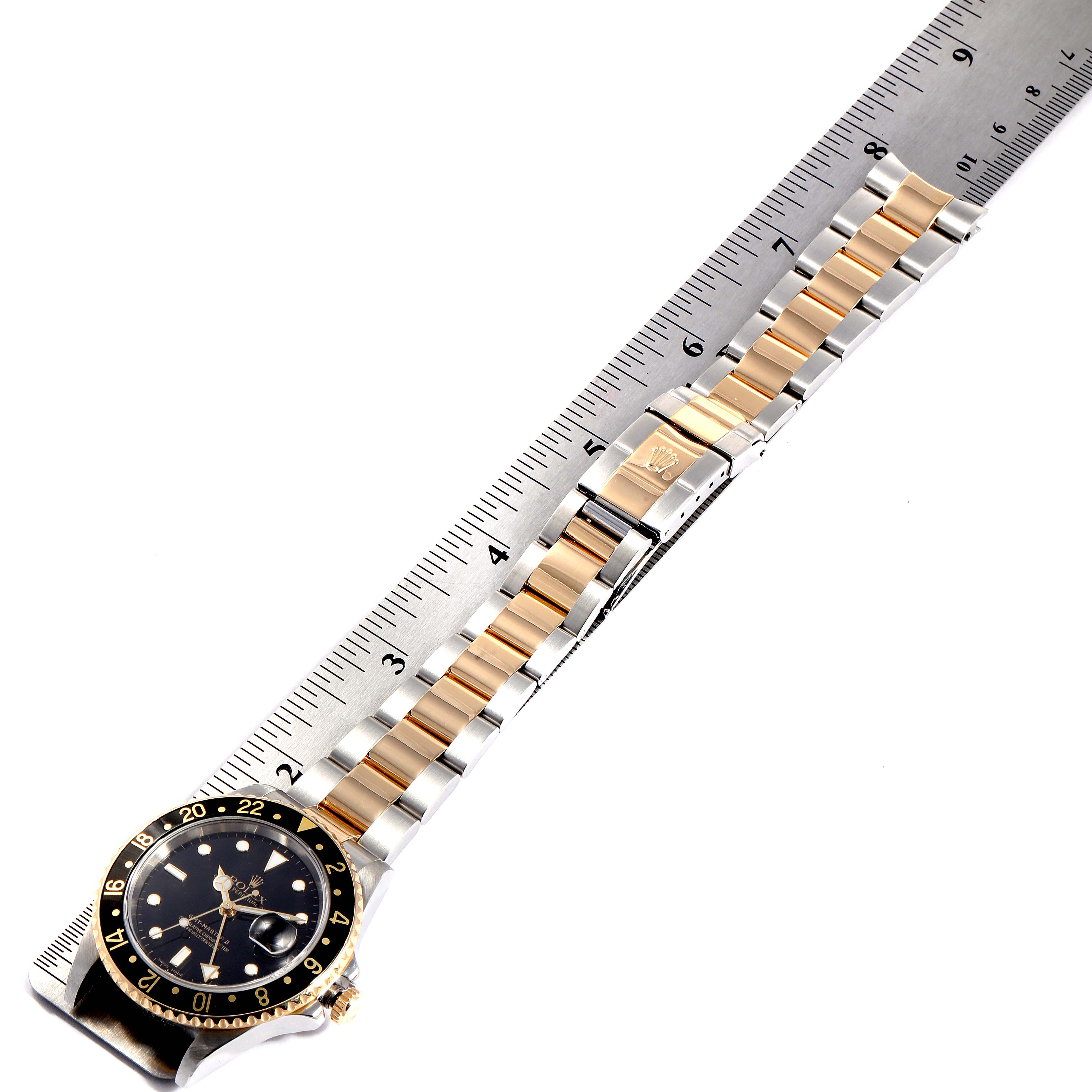 The image shows a full view of a Rolex GMT-Master 16713 Men's Steel and Gold (two tone) Black Dial 16713 Men's Steel and Gold (two tone) Black Dial watch, featuring the bezel, dial, bracelet, and clasp, alongside a ruler.