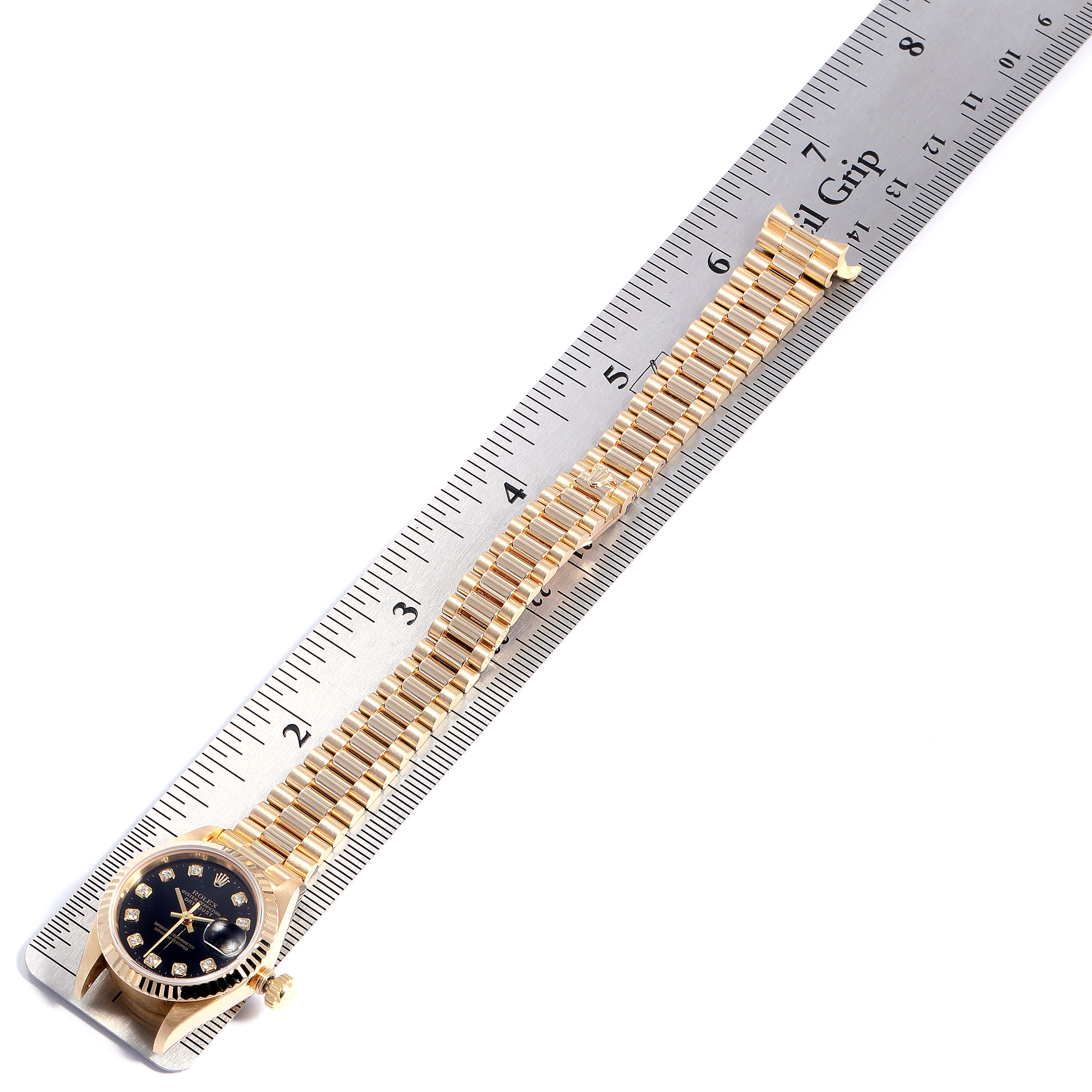 The image shows a Rolex President 69178 Women's Yellow Gold Black Dial 69178 Women's Yellow Gold Black Dial model watch placed on a ruler, displaying the watch head and partially extended bracelet.