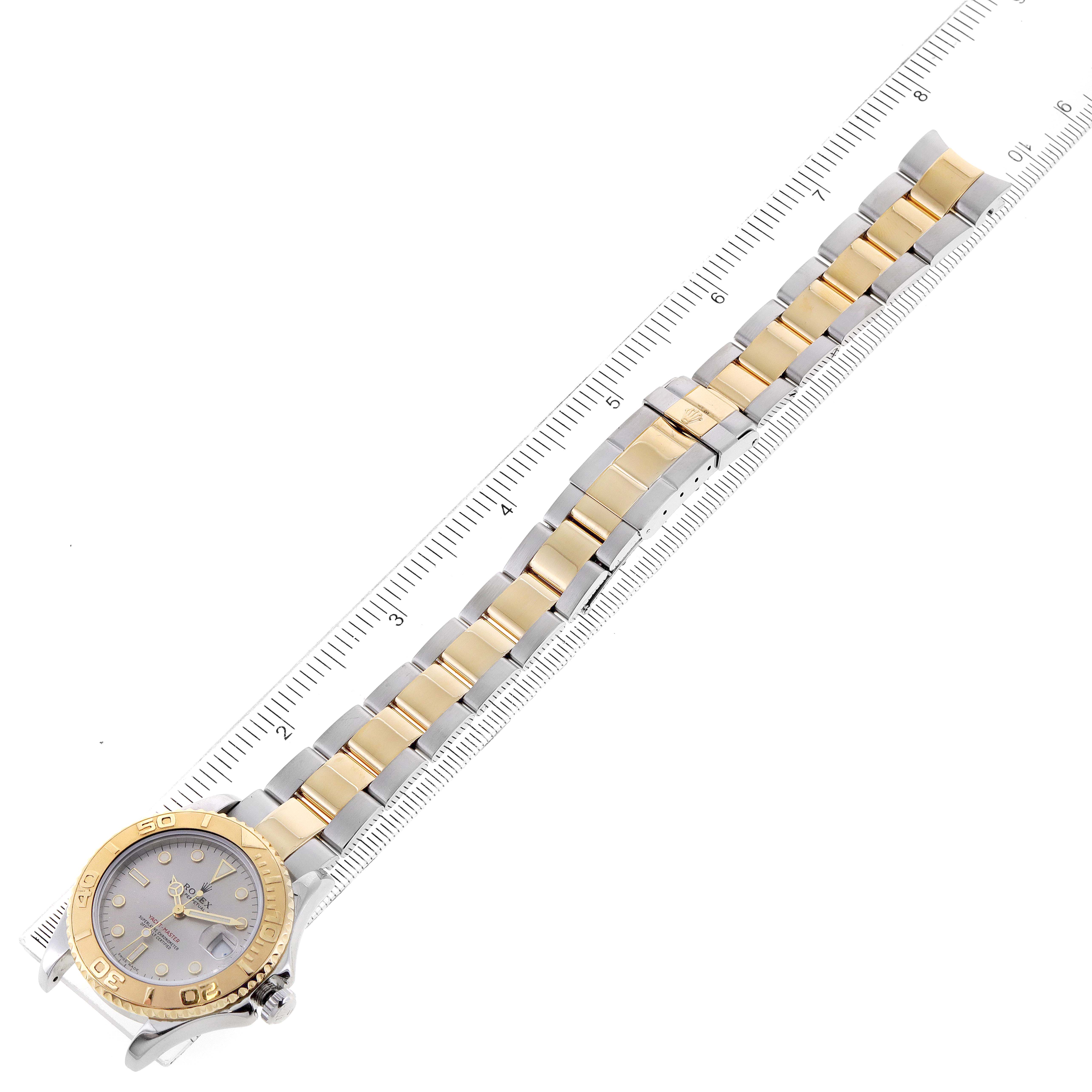This image shows a Rolex Yacht-Master 168623 Women's Steel and Gold (two tone) Grey Dial 168623 Women's Steel and Gold (two tone) Grey Dial watch laid flat with a gold and silver band next to a ruler for scale.