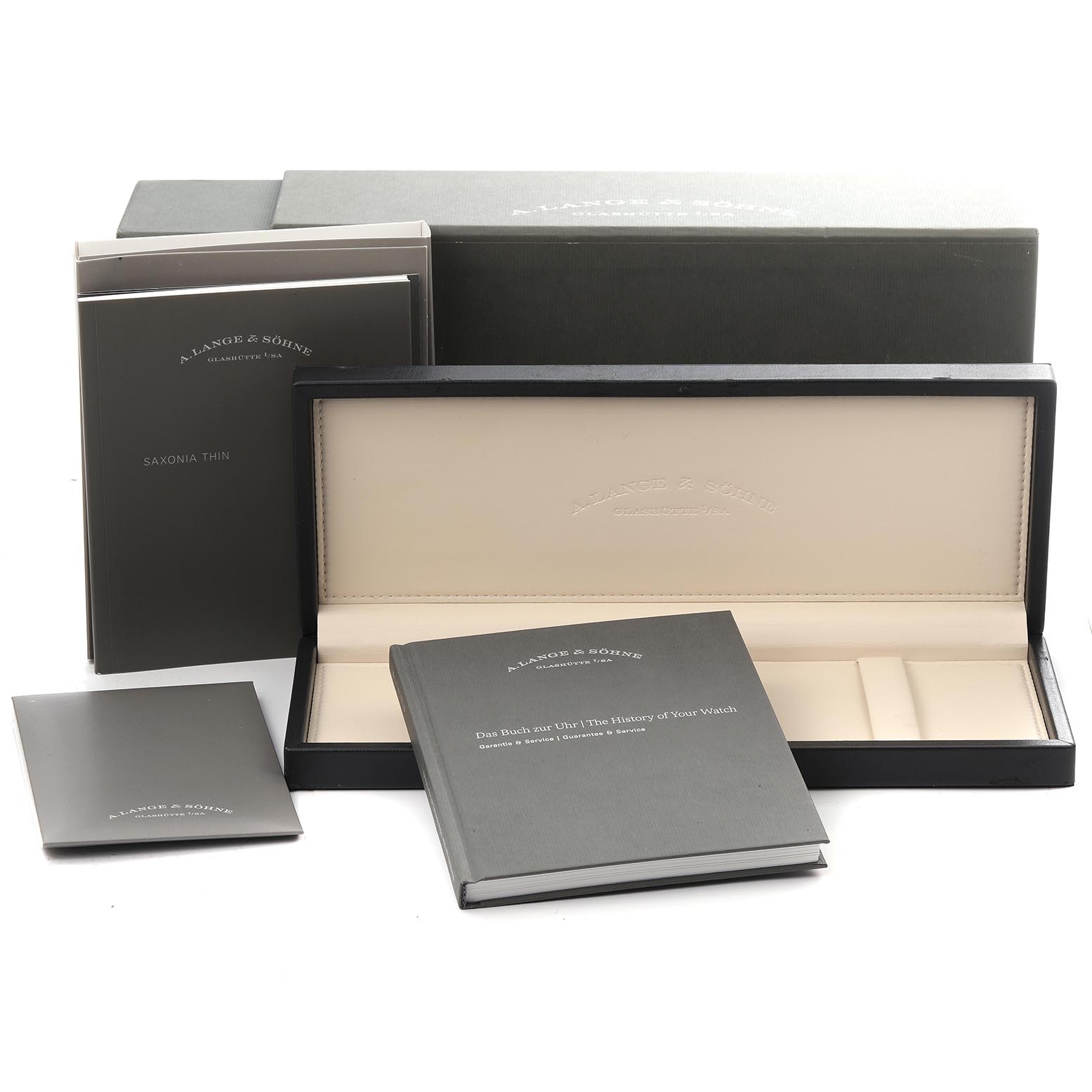 The image shows a Saxonia model watch box and accessories by A. Lange & Söhne, including manuals and an empty watch case.