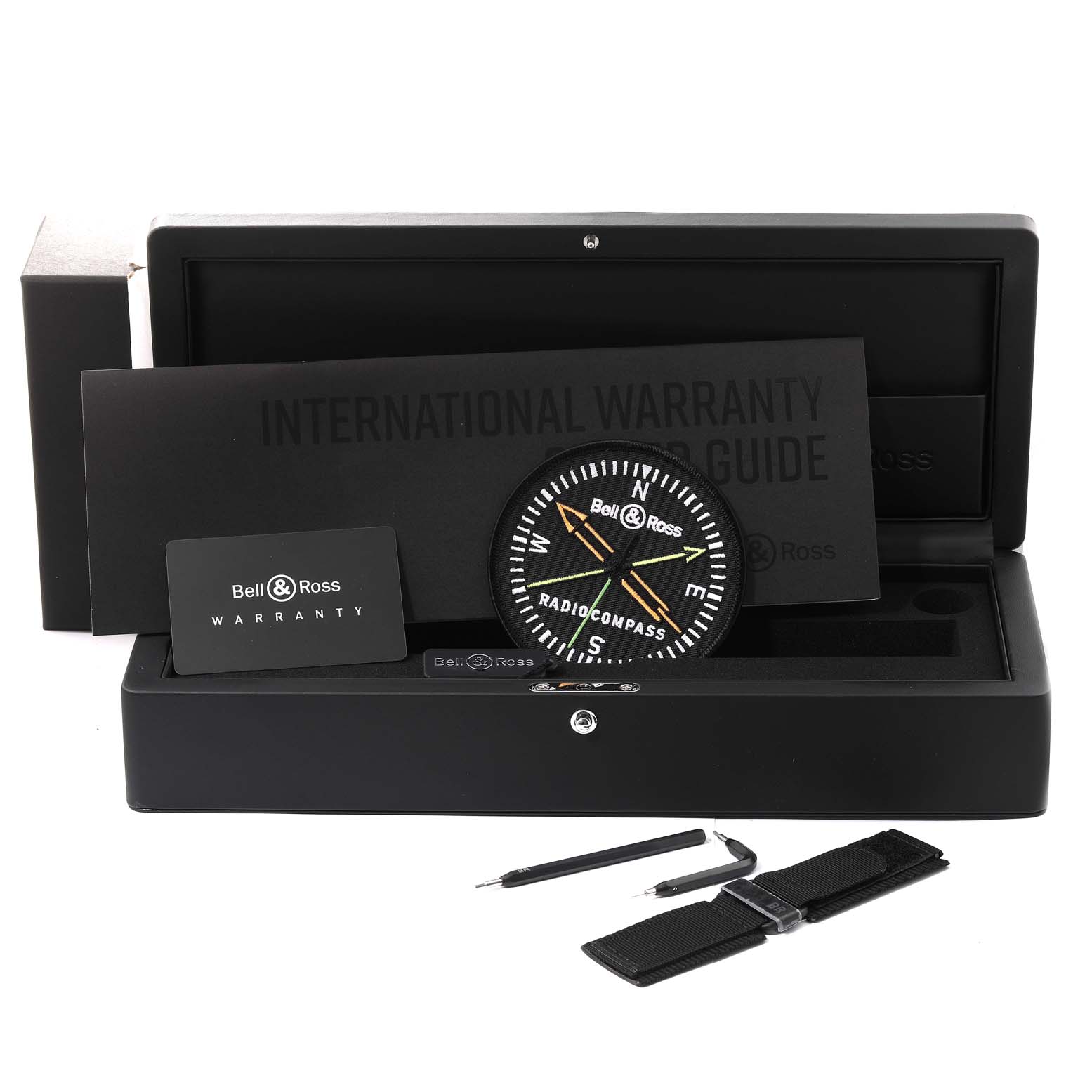 The image shows the Bell 
Ross Instruments BR0392-RCO-CE/SRB Men
s Ceramic Black Dial BR0392-RCO-CE/SRB Men
s Ceramic Black Dial model watch at a front angle, along with its warranty card, guide, tools, and strap in a box.