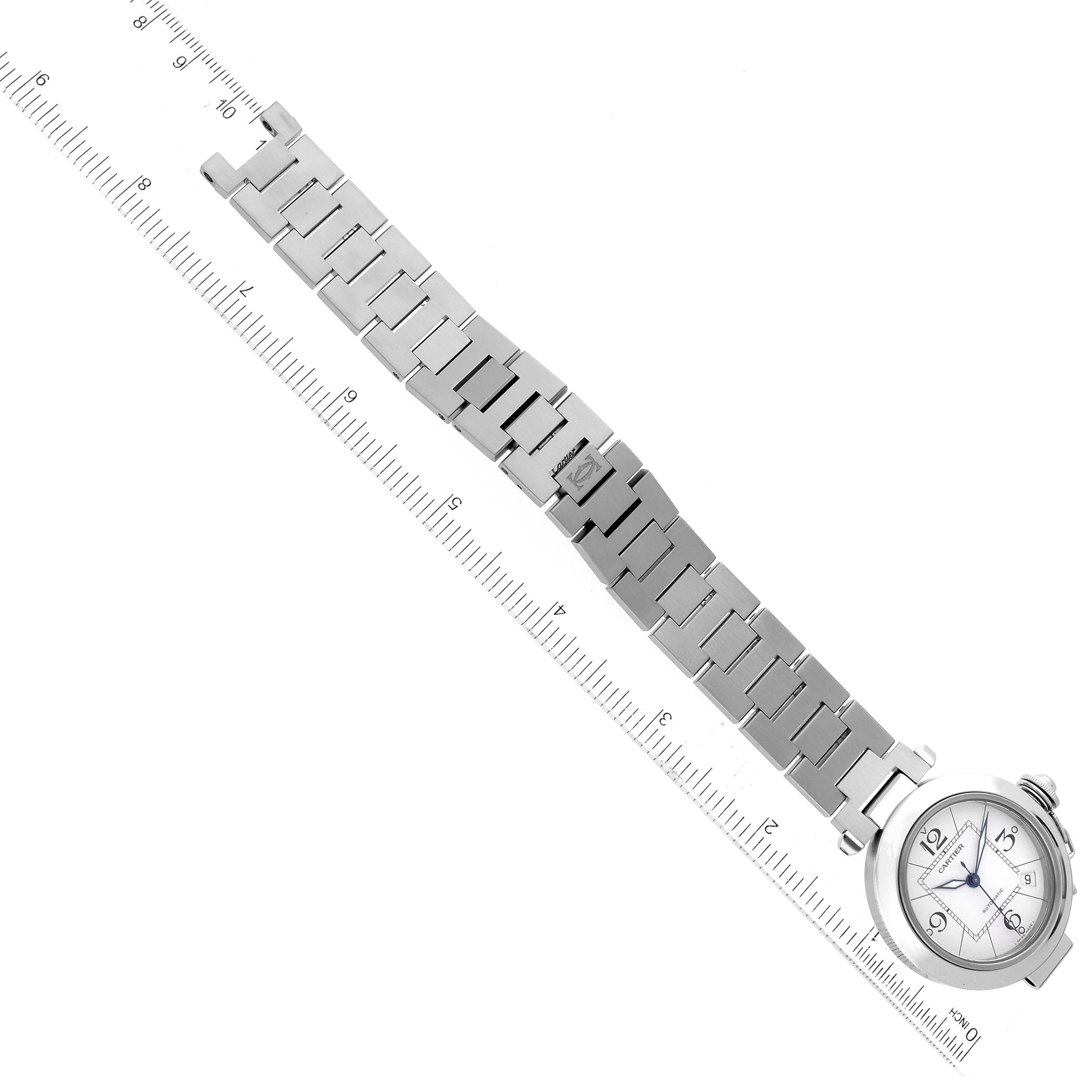 The Cartier Pasha W31074M7 Men's Stainless Steel White Dial W31074M7 Men's Stainless Steel White Dial watch is shown from a top-down angle, highlighting its bracelet, clasp, and watch face, alongside a ruler for scale.
