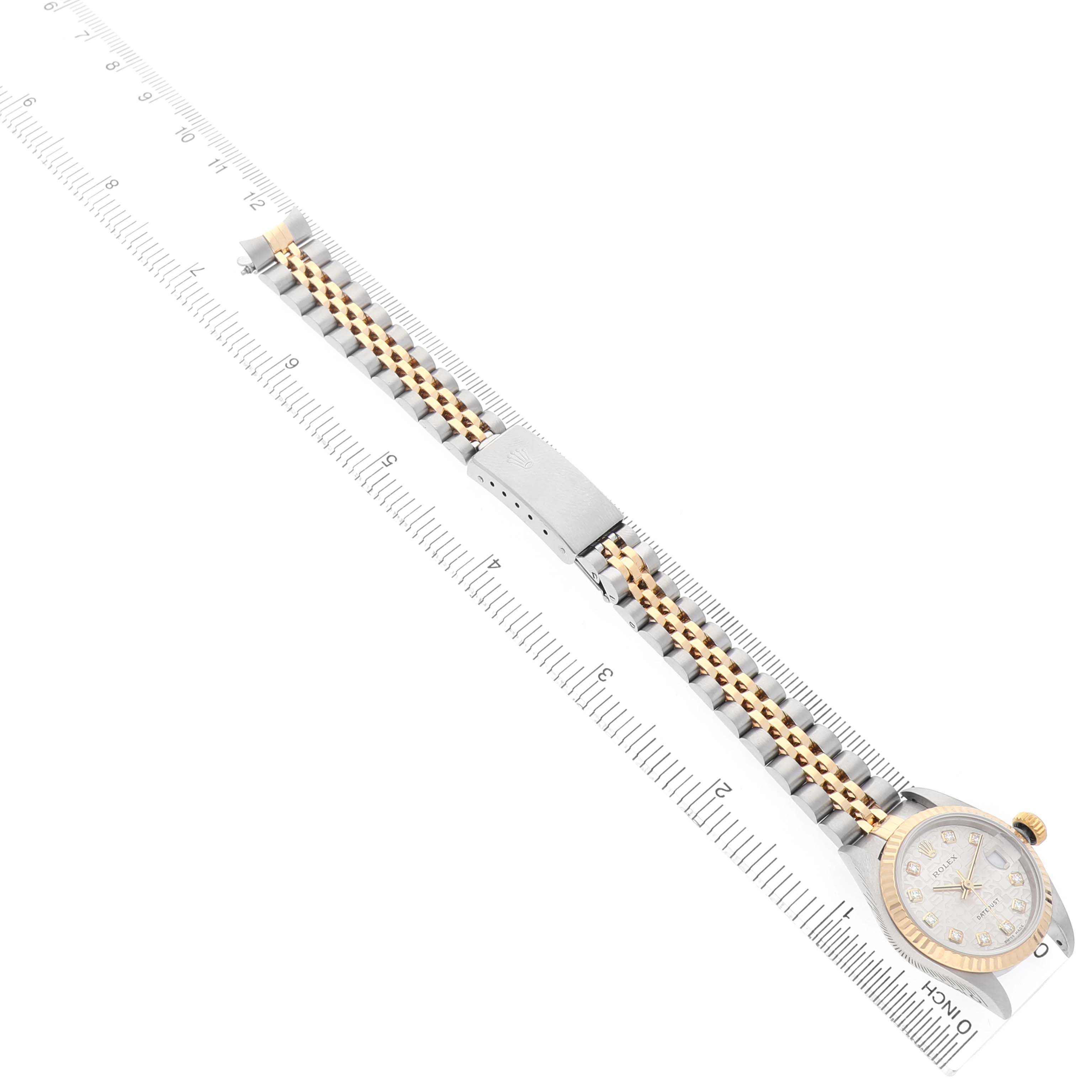 The Rolex Datejust 79173 Women's Steel and Gold (two tone) Silver Dial watch is shown lying flat, displaying the face, two-tone bracelet, and clasp alongside a ruler.