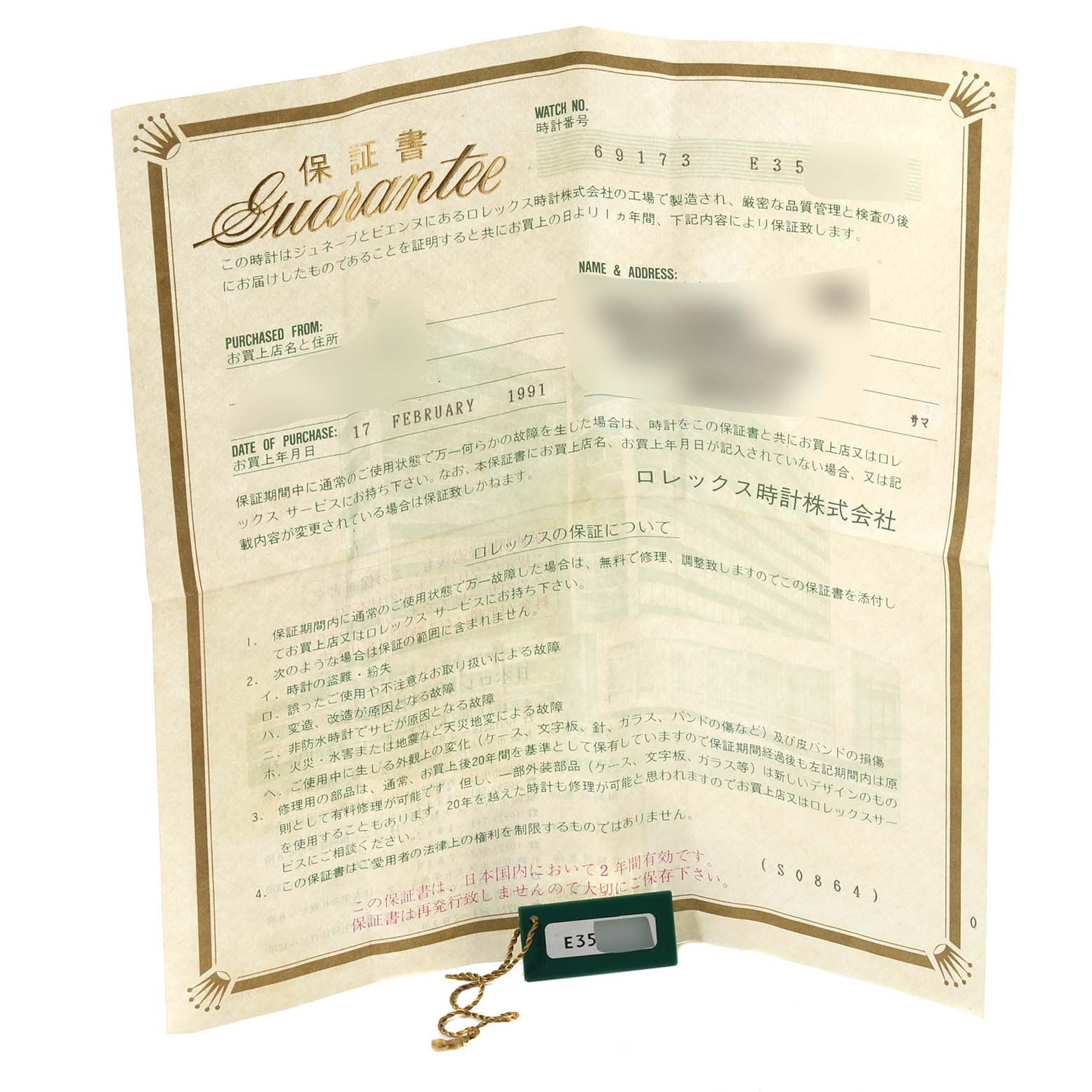 This image shows a Rolex Datejust 69173 Women's Steel and Gold (two tone) Champagne Dial 69173 Women's Steel and Gold (two tone) Champagne Dial guarantee certificate and a green tag with a chain, both laid flat.