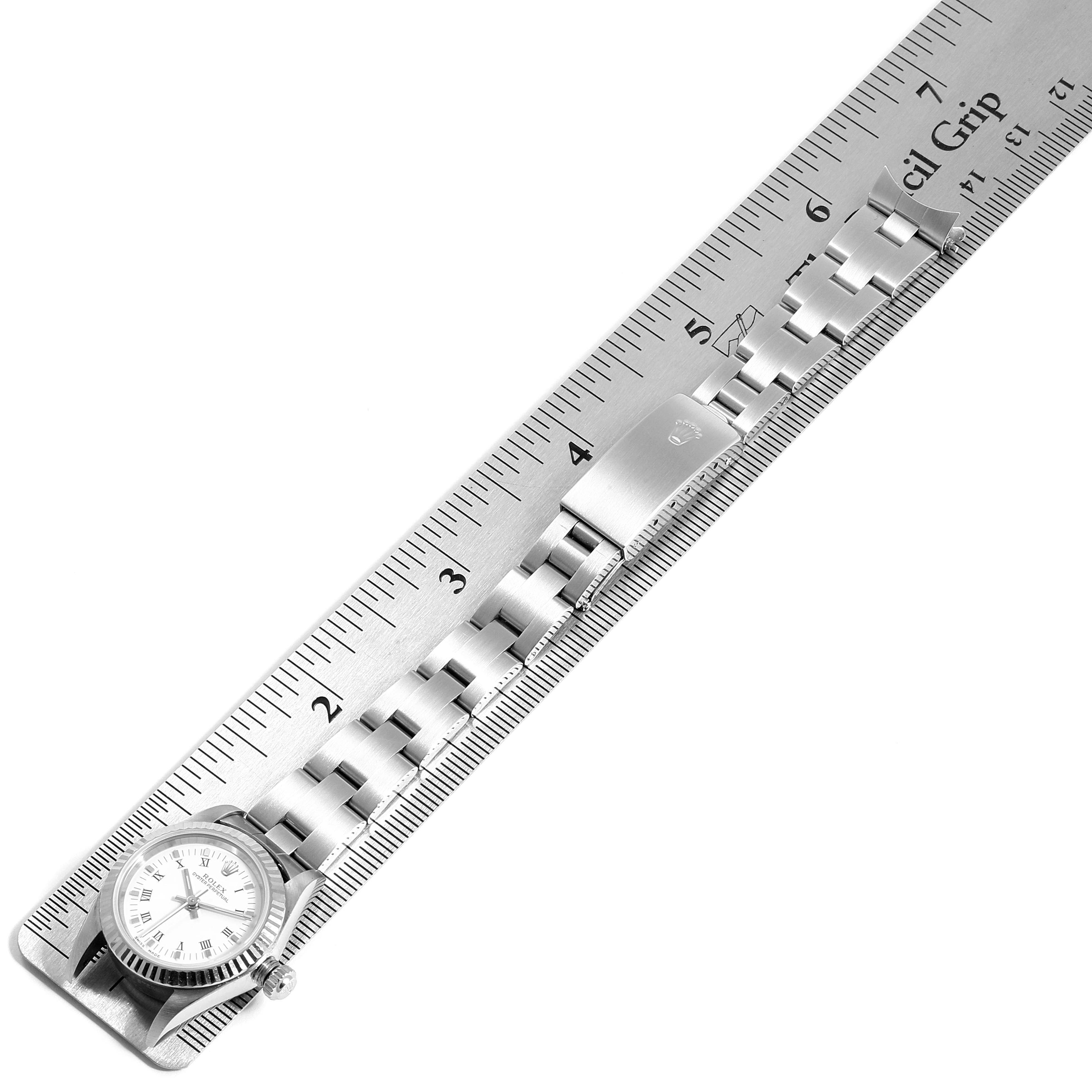 The image shows the Rolex Oyster Perpetual 76094 Women
s Stainless Steel White Dial 76094 Women
s Stainless Steel White Dial watch laid flat alongside a metal ruler, displaying its bracelet and clasp.