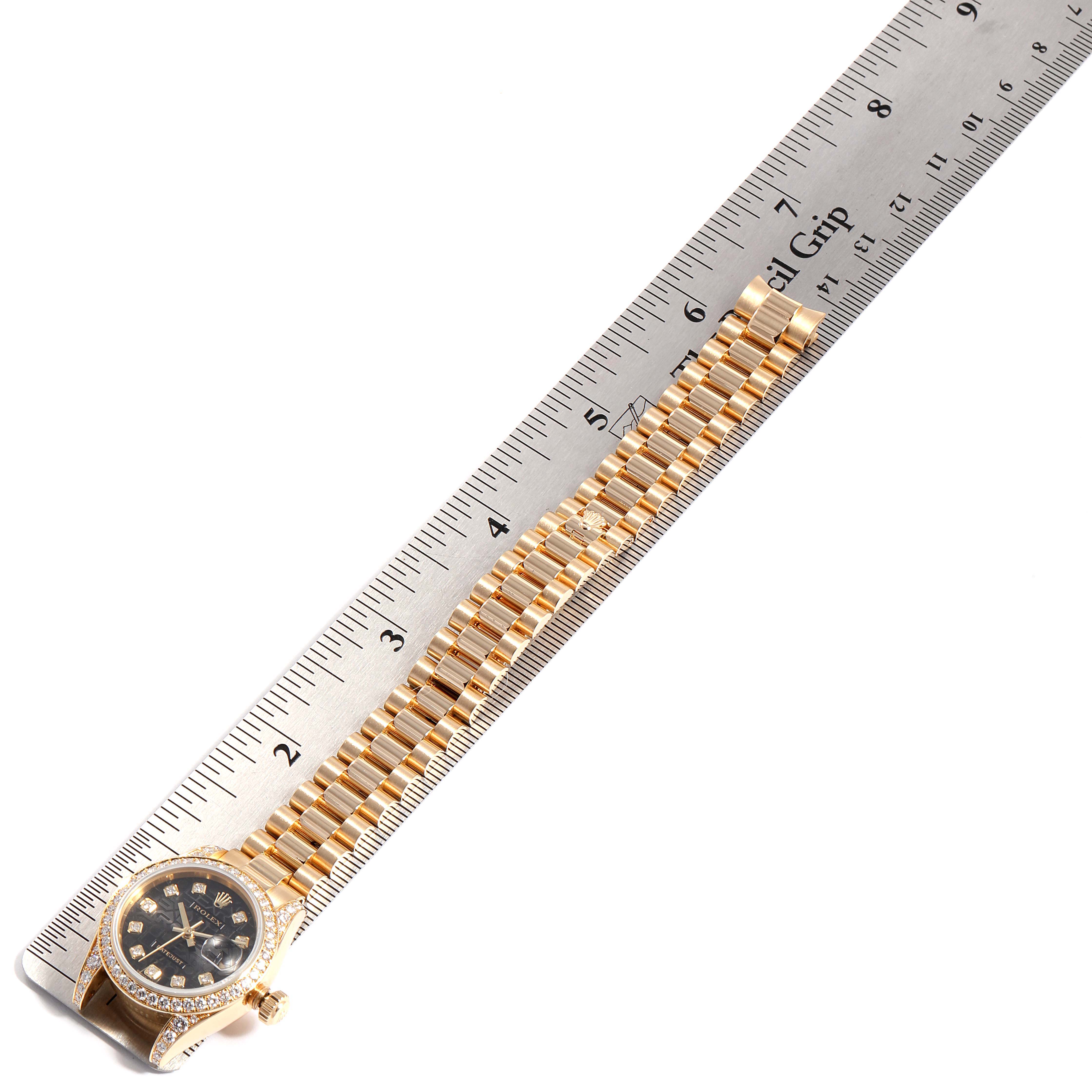 The Rolex President 179158 Women's Yellow Gold Black Dial 179158 Women's Yellow Gold Black Dial model watch is shown from a top-down angle, featuring the dial and full length of the bracelet next to a ruler.