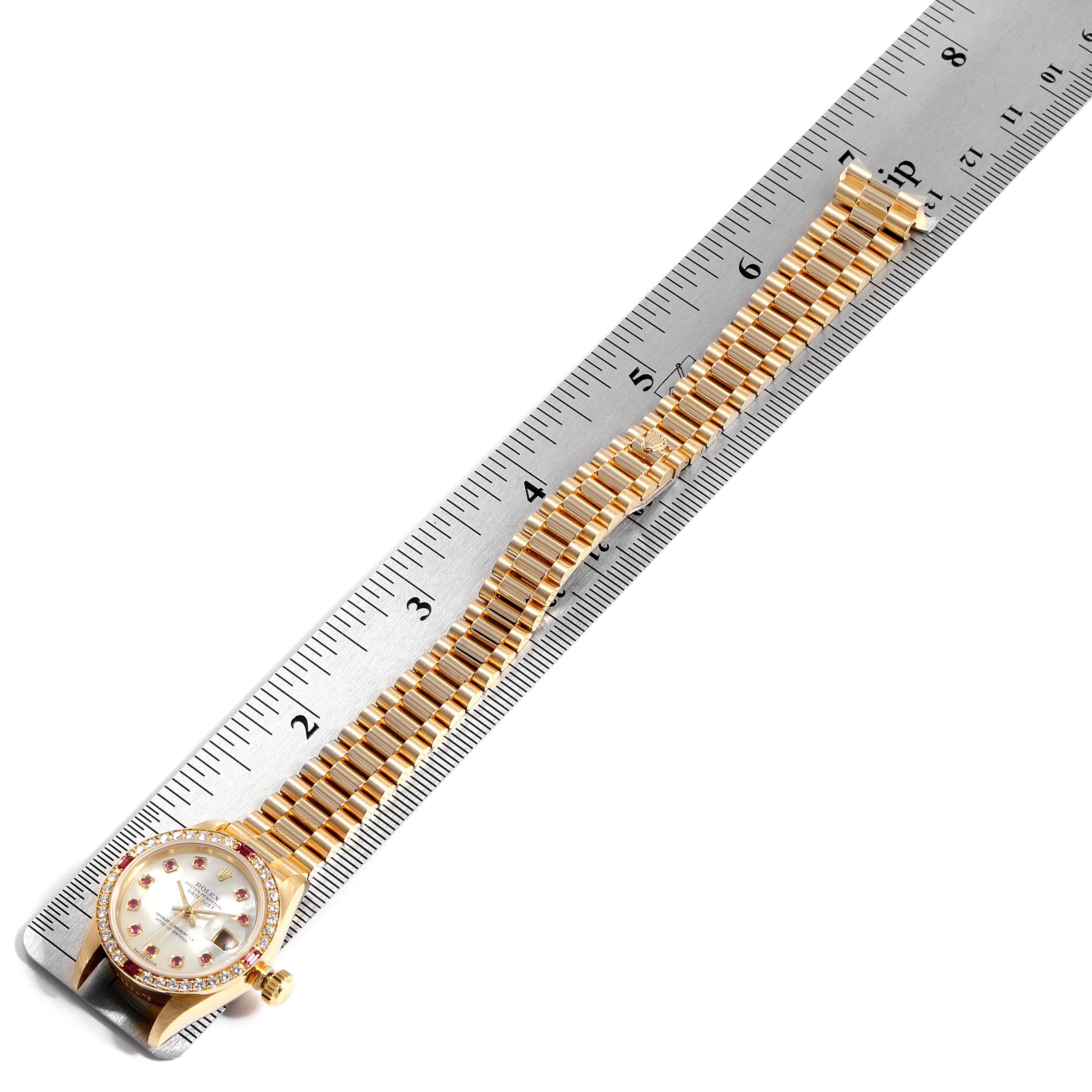 The image shows a Rolex President 69068 Women
s Yellow Gold Mother of Pearl Dial 69068 Women
s Yellow Gold Mother of Pearl Dial model watch placed alongside a ruler, displaying its gold bracelet and watch face from a top-down angle.