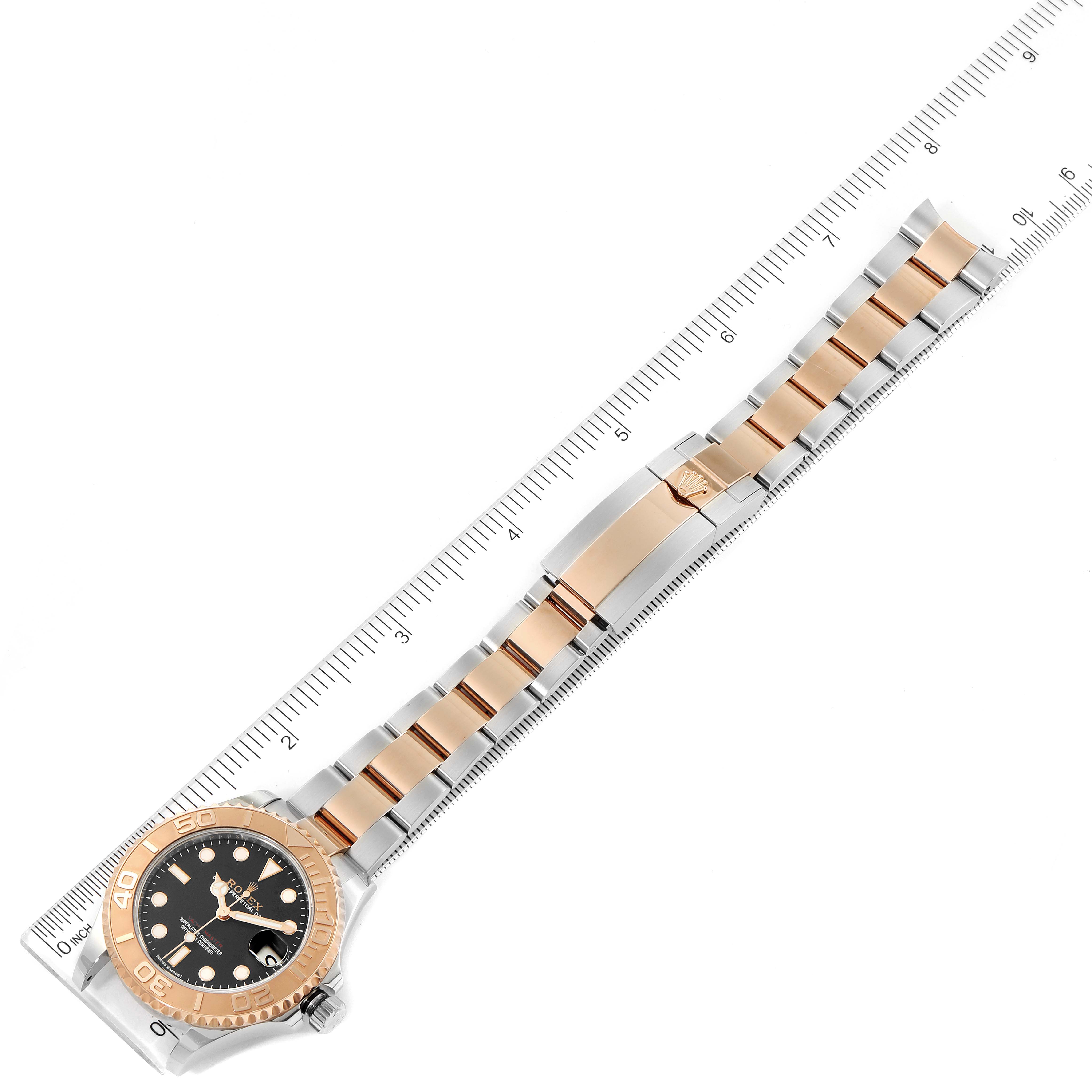The Rolex Yacht-Master 268621 Men
s Steel and Gold (two tone) Black Dial 268621 Men
s Steel and Gold (two tone) Black Dial watch is shown from above, displaying its face and the full length of its bracelet with a ruler for scale.