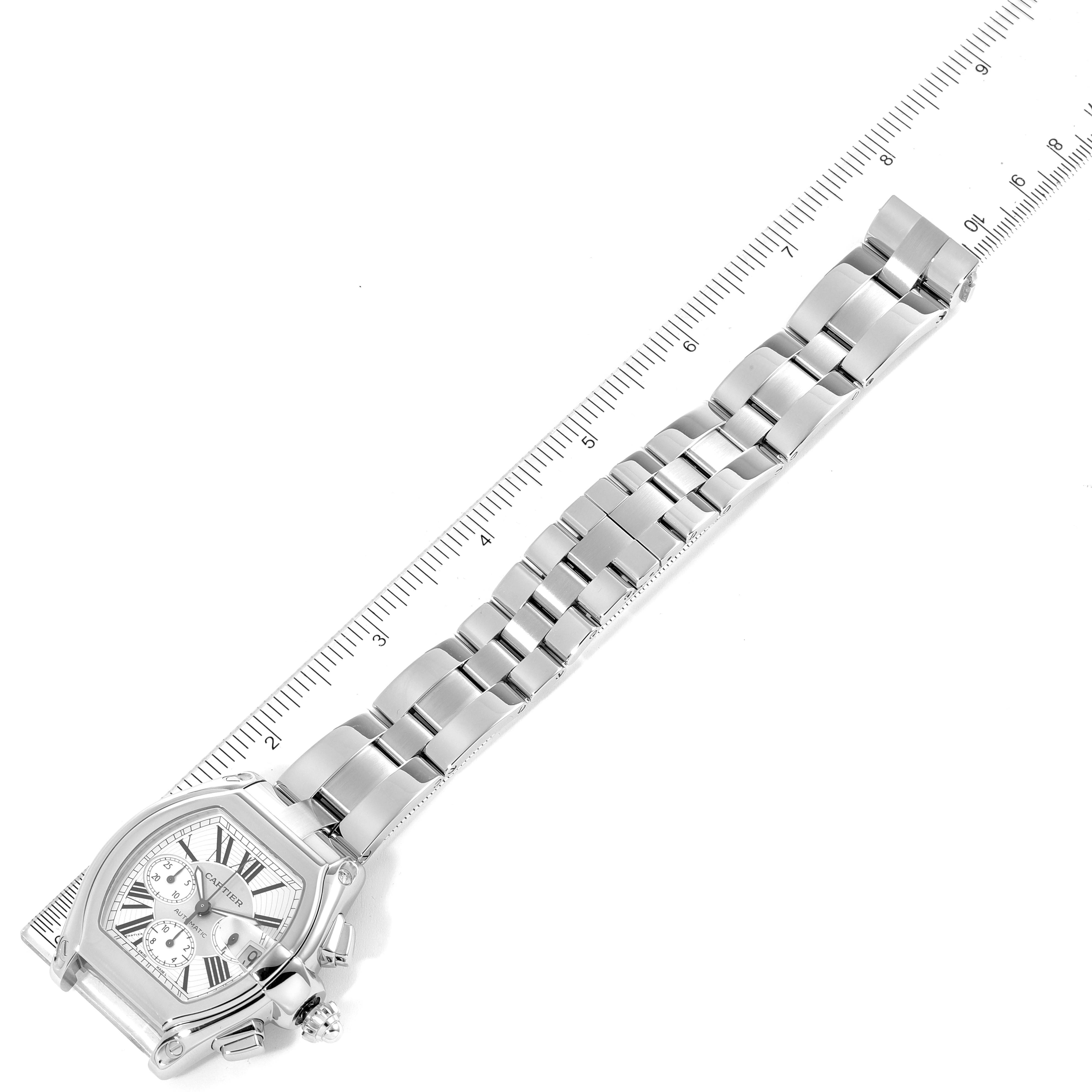 The image shows the Cartier Roadster W62019X6 Men
s Stainless Steel Silver Dial W62019X6 Men
s Stainless Steel Silver Dial watch laid flat with a ruler beneath it, displaying its bracelet and face.
