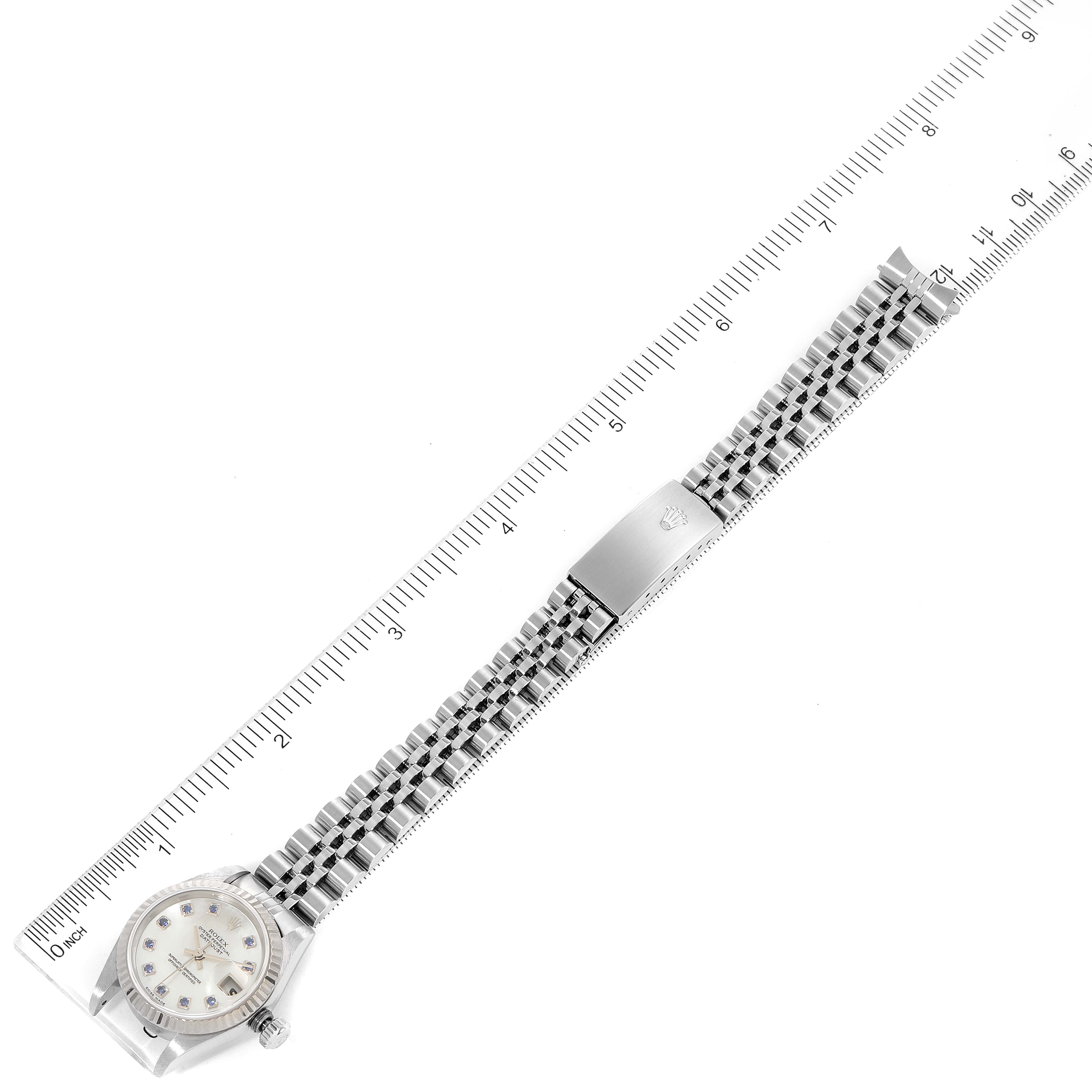 The image shows a Rolex Datejust 79174 Women
s Stainless Steel Mother of Pearl Dial 79174 Women
s Stainless Steel Mother of Pearl Dial watch laid flat with the bracelet fully extended and a ruler positioned alongside it.