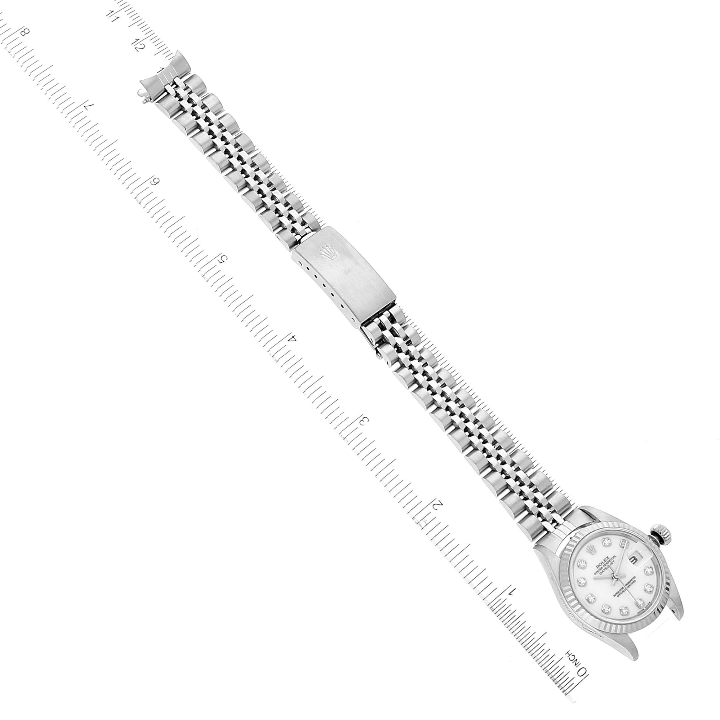 The image shows a top-down view of a Rolex Datejust 79174 Women's Stainless Steel White Dial 79174 Women's Stainless Steel White Dial watch with its bracelet and clasp extended next to a ruler.