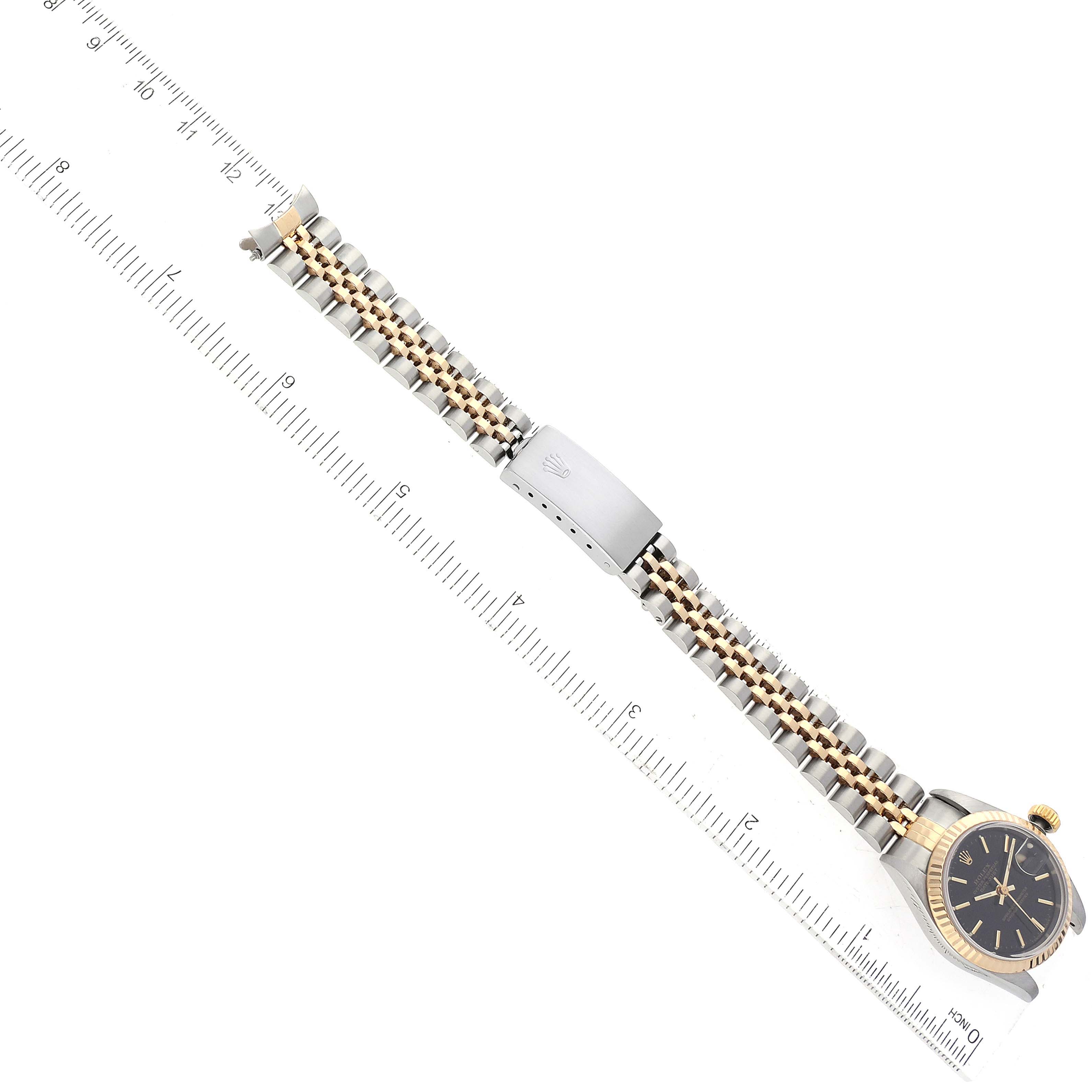 The image shows a Rolex Datejust 69173 Women's Steel and Gold (two tone) Black Dial 69173 Women's Steel and Gold (two tone) Black Dial watch laid flat, showcasing the watch face and metal bracelet with a clasp against a ruler for scale.