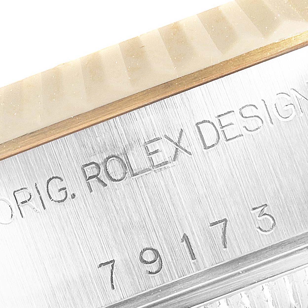 This close-up of the Rolex Datejust 79173 Women
s Steel and Gold (two tone) Silver Dial 79173 Women
s Steel and Gold (two tone) Silver Dial watch shows the engraved model number and part of the fluted bezel.