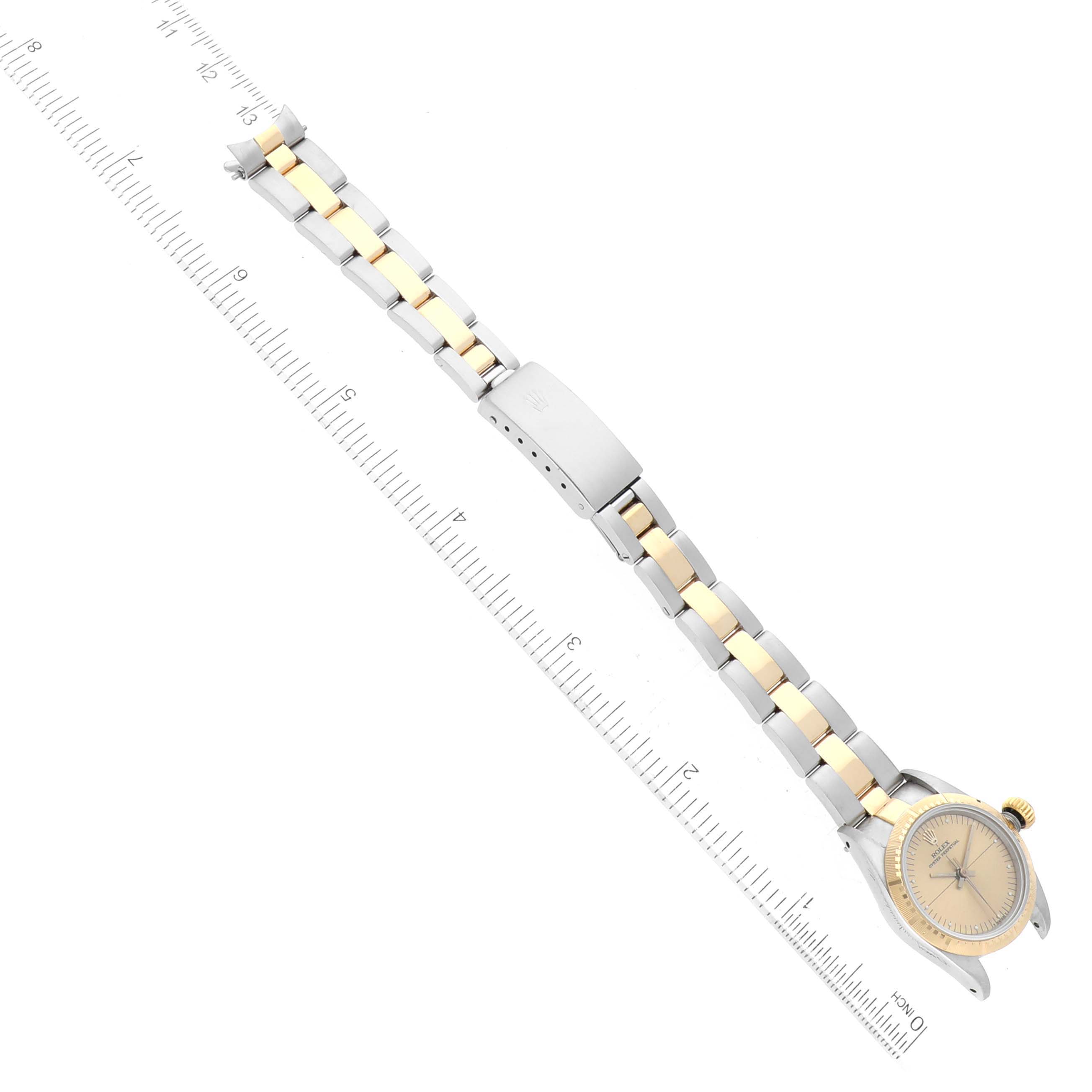 The image shows the Rolex Oyster Perpetual 67243 Women's Steel and Gold (two tone) Champagne Dial 67243 Women's Steel and Gold (two tone) Champagne Dial watch from a top-down angle, displaying its bracelet, clasp, and watch face next to a ruler.