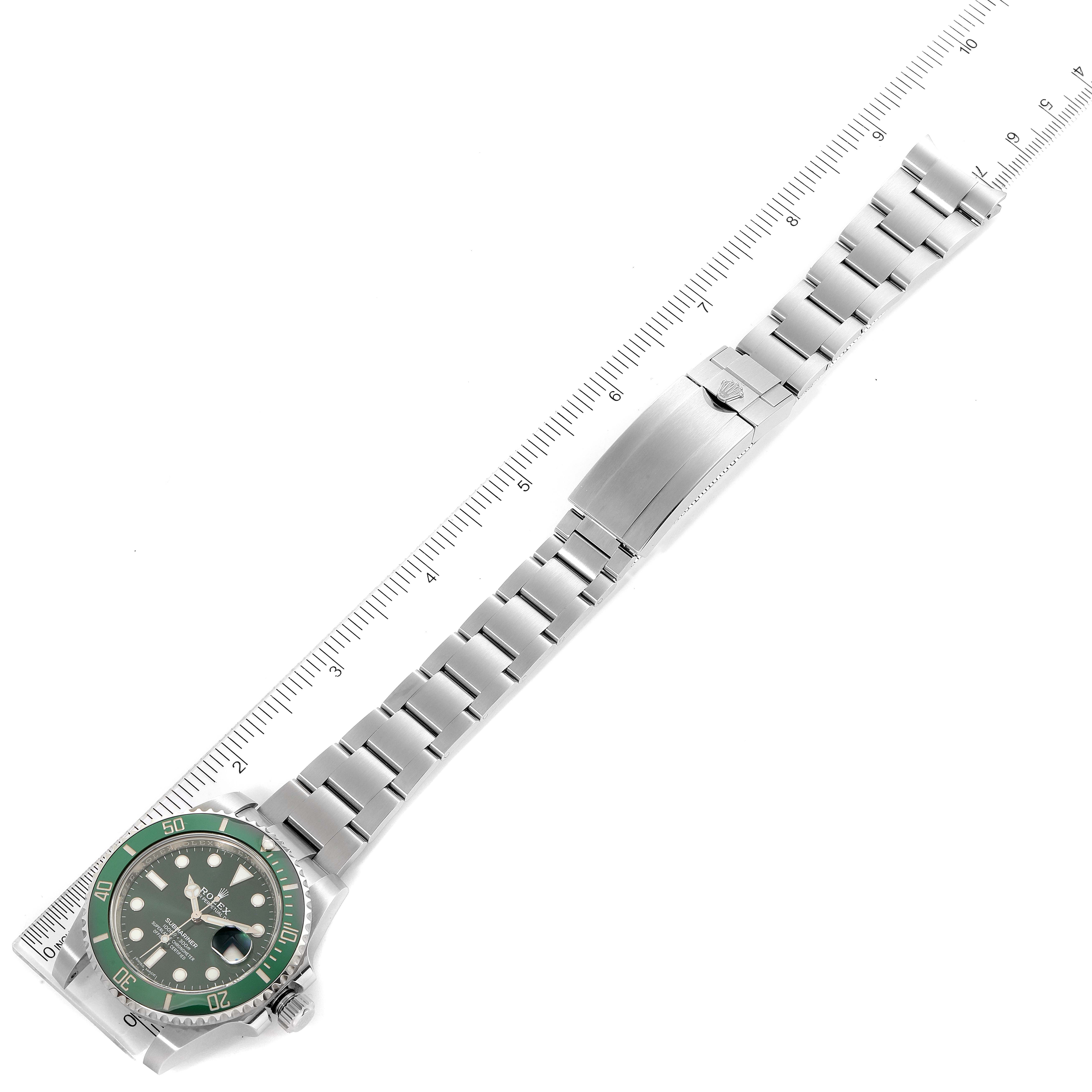 The image shows a top view of a Rolex Submariner 116610LV Men
s Stainless Steel Green Dial 116610LV Men
s Stainless Steel Green Dial watch with a green bezel and a stainless steel bracelet next to a ruler.