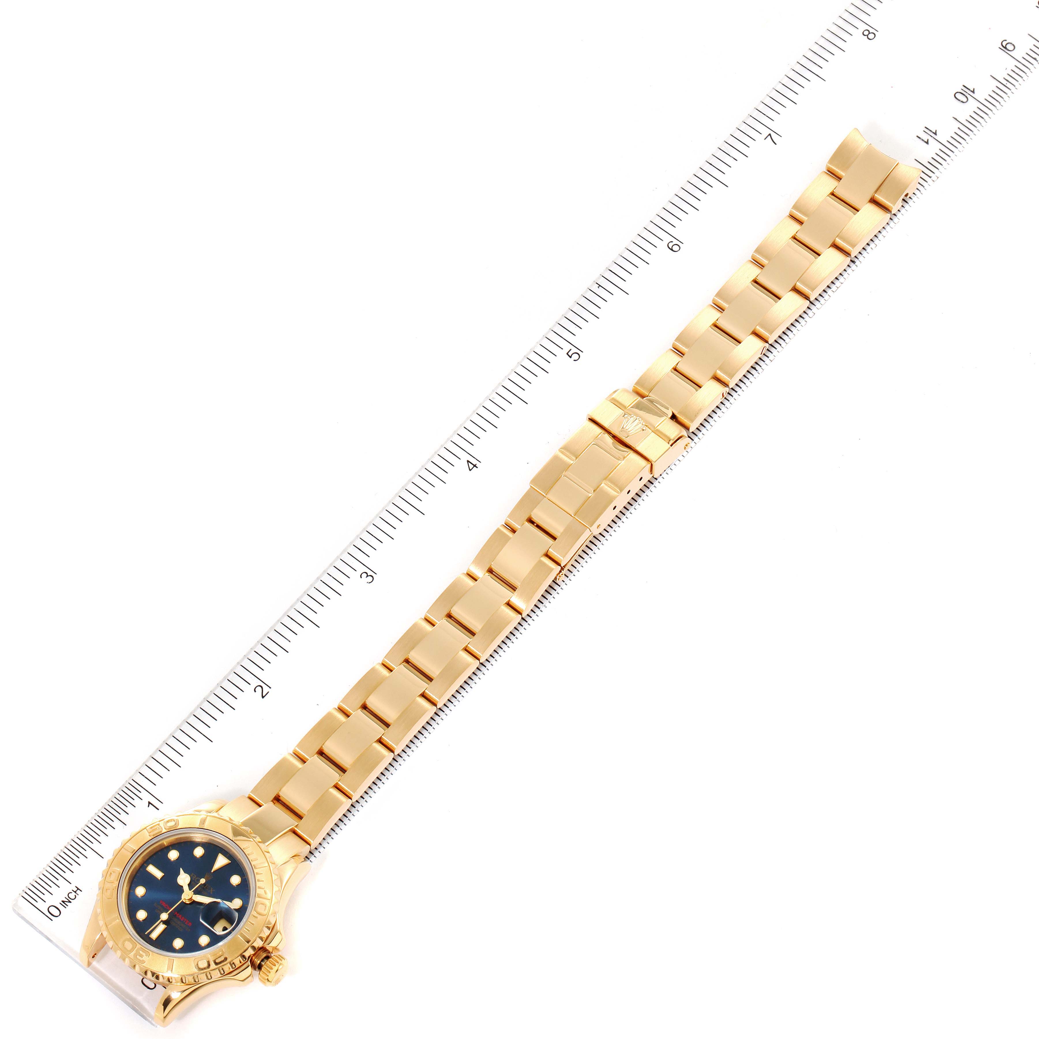 The image shows a top view of the Rolex Yacht-Master 69628 Women's Yellow Gold Blue Dial 69628 Women's Yellow Gold Blue Dial watch along with its gold bracelet aligned next to a measuring ruler.
