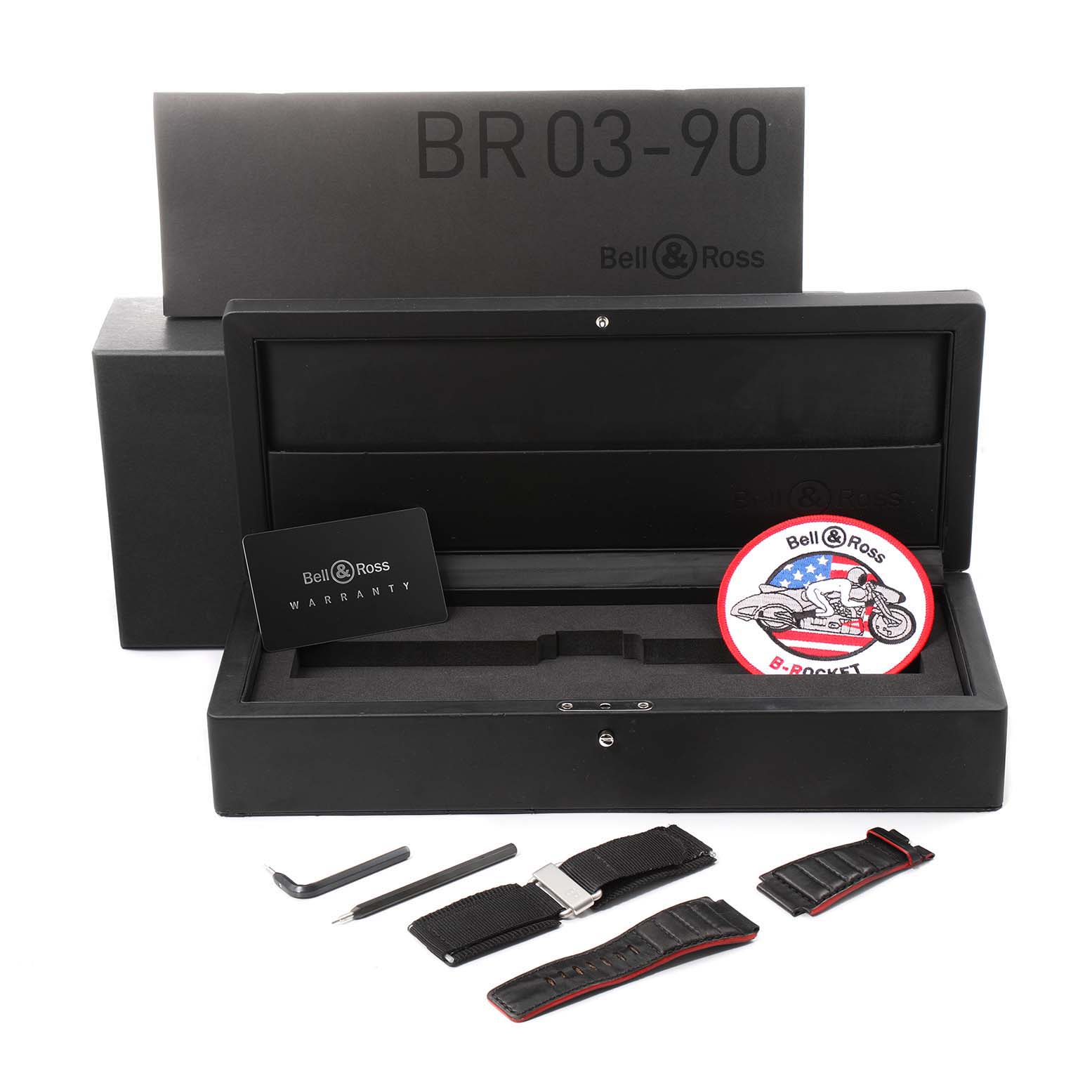 The image shows the packaging, additional straps, tools, a warranty card, and a patch for the Bell & Ross Rocket Grande Date Power Reserve Steel Watch BR0390 Unworn model.